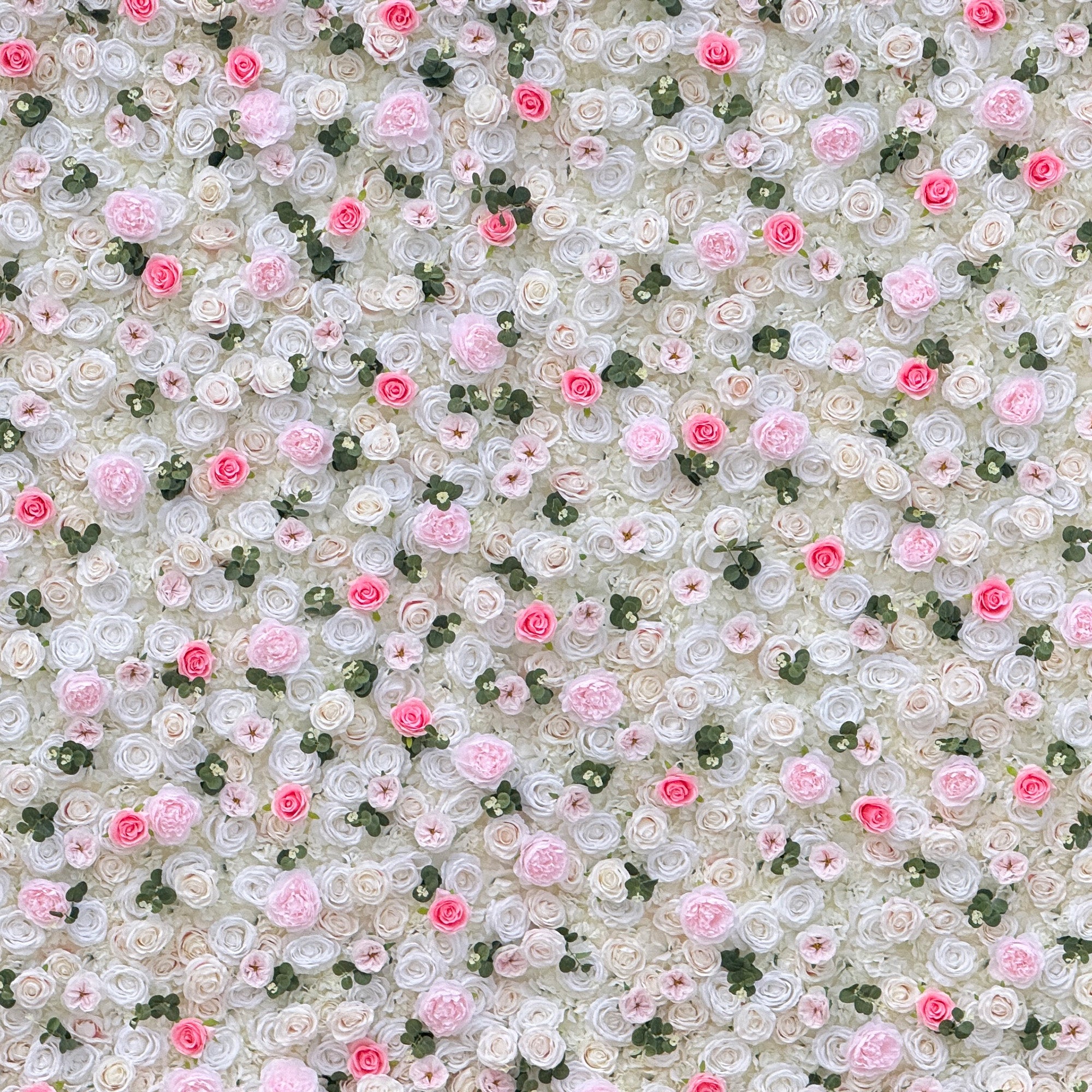 This photo showcases a stunning floral wall, likely by ValarFlowers, featuring artificial roses in soft pink and white hues, interspersed with greenery. The dense arrangement creates a romantic and elegant ambiance, perfect for weddings or other formal events. The realistic appearance of the faux flowers adds a touch of timeless beauty, making it an ideal backdrop for capturing memorable moments with a dreamy, celebratory atmosphere.