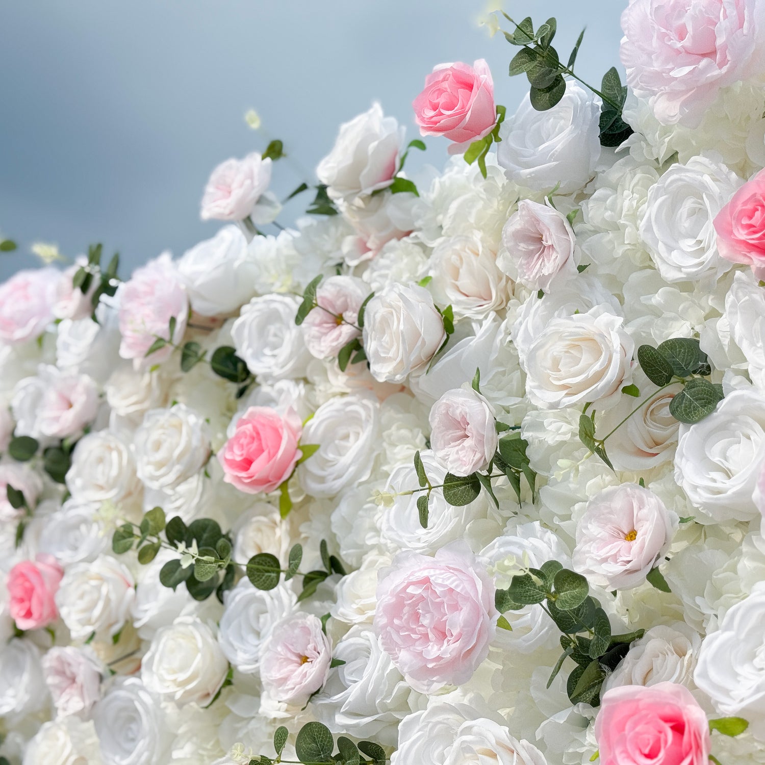This photo features a lush floral wall, likely by ValarFlowers, with artificial roses in soft pink and white, plus greenery. The dense arrangement creates a romantic, elegant vibe, perfect for weddings. The realistic faux flowers add timeless beauty, ideal for capturing memorable moments with a dreamy, celebratory feel.