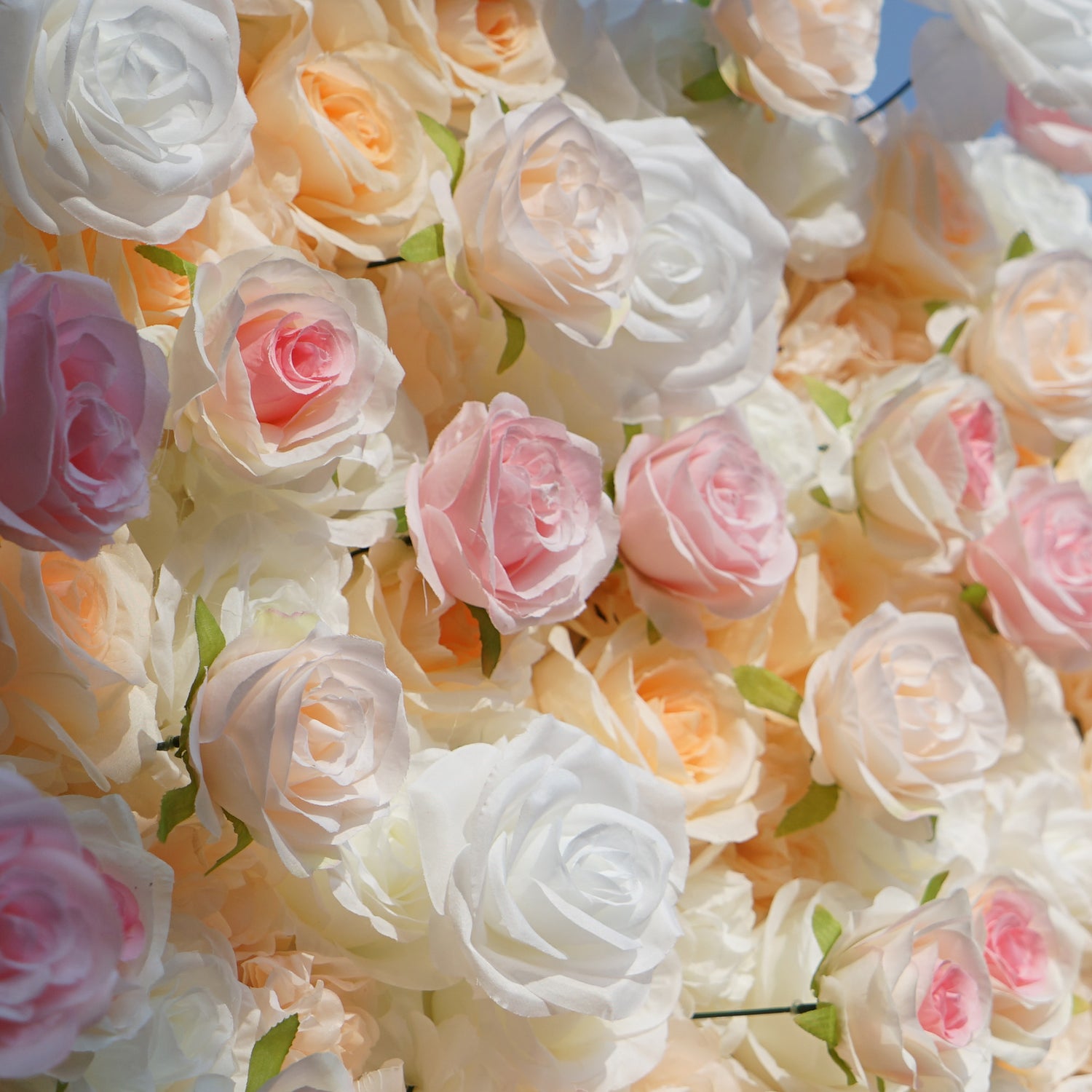 This photo showcases a lush floral wall composed of artificial roses, likely by ValarFlowers. The blooms come in soft shades of white, peach, and pink, creating a romantic and elegant aesthetic. This setup is perfect for events like weddings, where the delicate hues and realistic appearance of the faux flowers add a touch of timeless beauty. The dense arrangement and pastel colors evoke a dreamy, celebratory atmosphere, making it an ideal backdrop for capturing memorable moments.