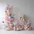 This set of floral decorations features a soft and dreamy color scheme with shades of pink, purple, and white. There are various artificial flowers such as roses, hydrangeas, and lilies, along with some delicate foliage. The large vertical arrangement and smaller pieces on the ground create a layered and romantic look, ideal for a wedding ceremony, bridal shower, or other elegant events.