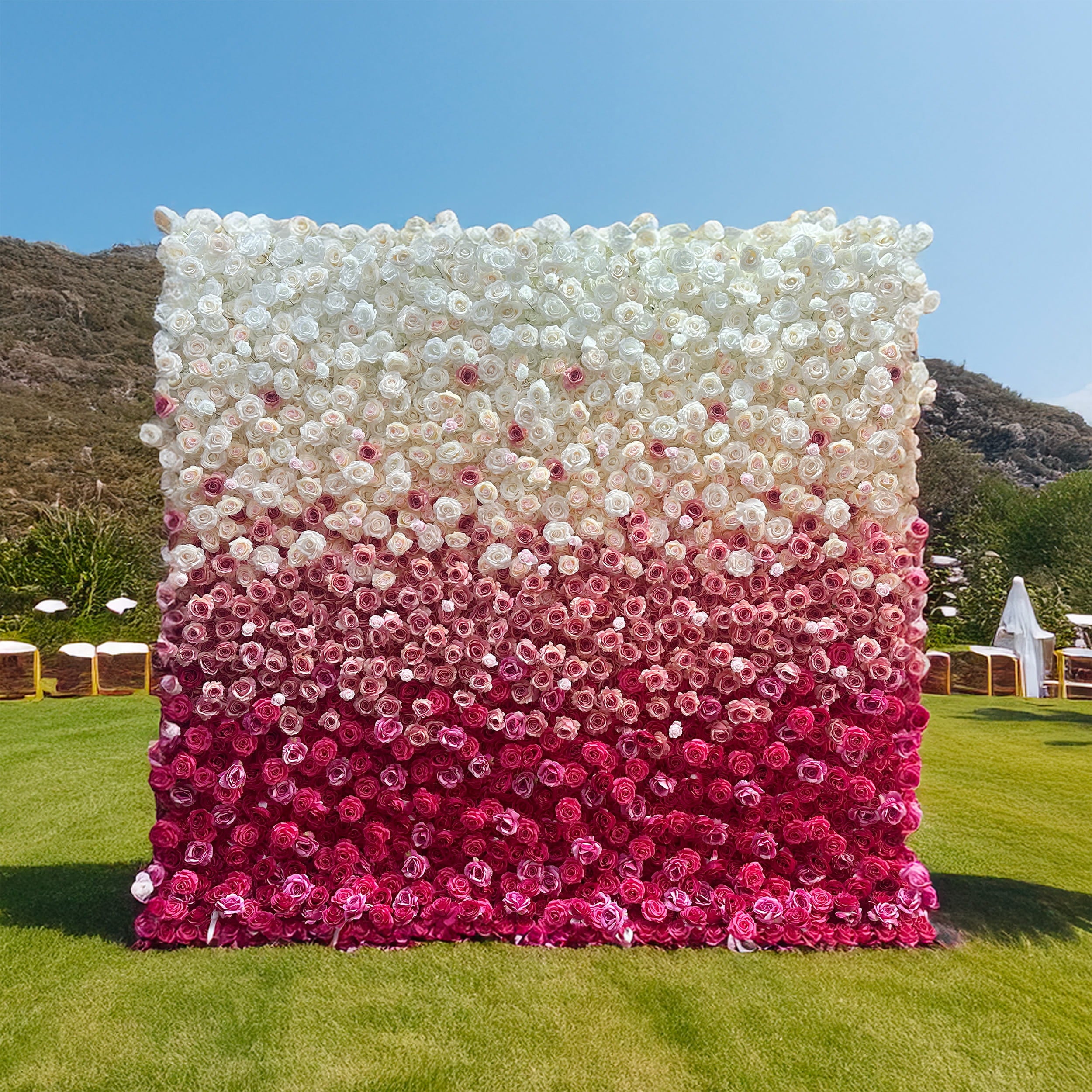 This image showcases a striking flower wall made of artificial flowers, set outdoors on a grassy area. The wall features a gradient design transitioning from white at the top to deep pink at the bottom, primarily composed of rose - like blooms. The color scheme creates a visually appealing ombre effect, exuding a romantic and elegant style, perfect for events such as weddings or photo - shoots.