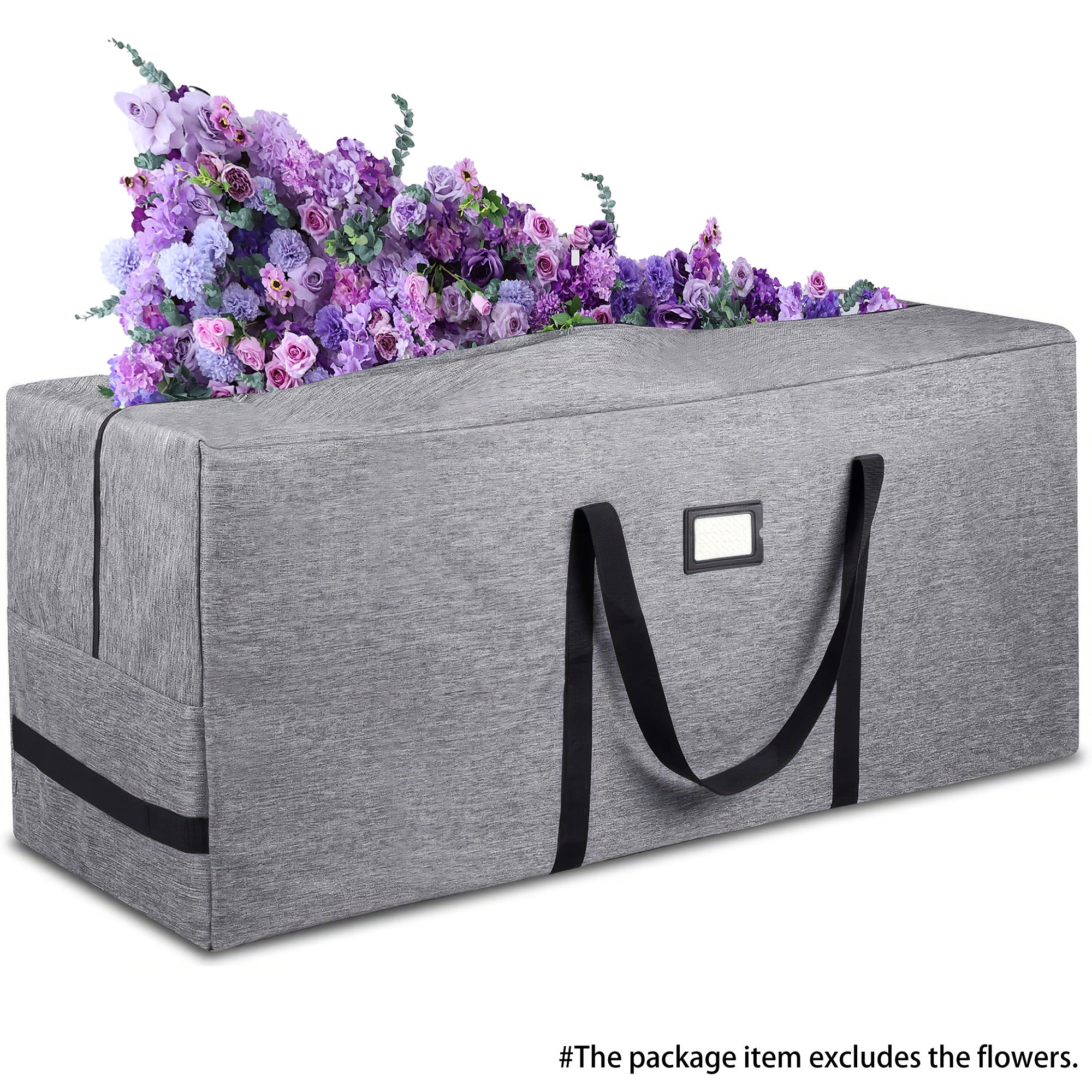 The image shows a rectangular storage bag with a textured fabric surface. The bag is available in a light gray color and features sturdy black handles on one side, along with a rectangular label patch. At the top of the bag, there is an arrangement of colorful artificial flowers in shades of purple, pink, and blue. A note at the bottom states, “The package item excludes the flowers,” indicating that the flowers are not part of the product being sold. The bag appears to be designed for practical storage, per