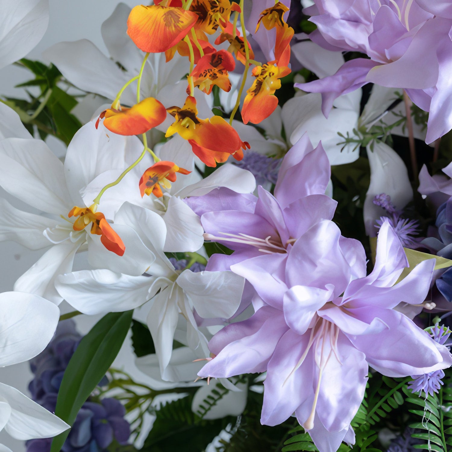 This image shows an artificial flower arrangement with a vibrant color palette of white, purple, and orange. It features large, broad - petaled white and purple flowers, along with small orange blooms, presenting a lively and exotic style.