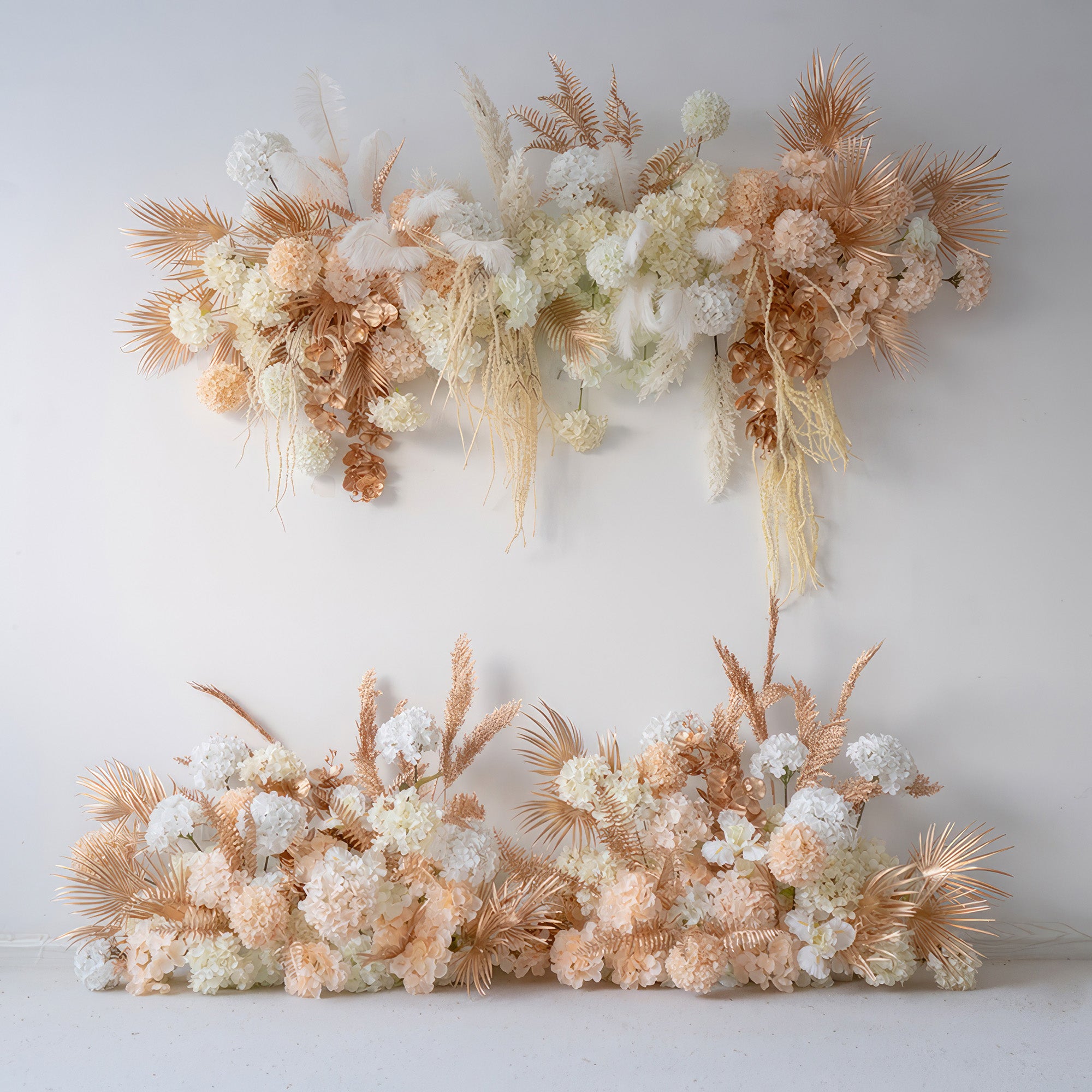 The image shows artificial floral decor with hydrangea - like flowers, palm fronds, and feathers. Colors are white, peach, and gold - toned, creating a luxurious, modern style perfect for event backdrops.