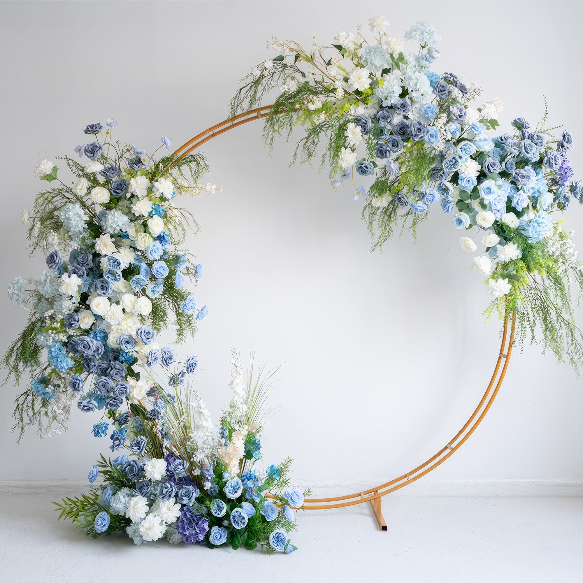 A sleek, gold circular floral arch from Valar Flowers, adorned with a serene palette of sky blue, dusty blue, and creamy white blooms—including roses, hydrangeas, and delicate baby&