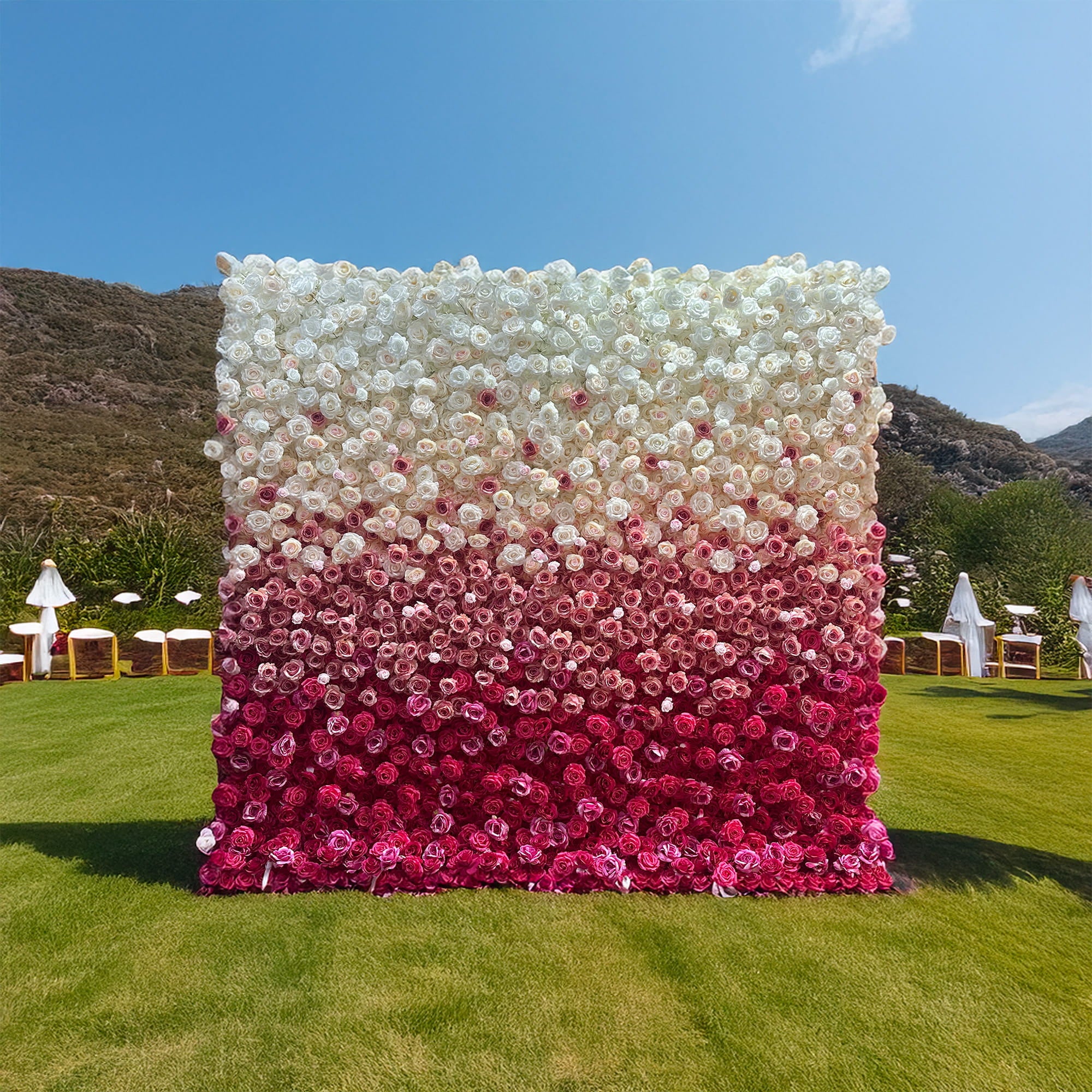 This image features a large, eye - catching flower wall set on a grassy outdoor area. The wall is densely packed with artificial roses, arranged in a gradient pattern. The colors transition smoothly from pure white at the top, through soft pinks, to deep magenta at the bottom. The style is elegant and romantic, perfect for events like weddings or upscale gatherings, creating a visually stunning backdrop.