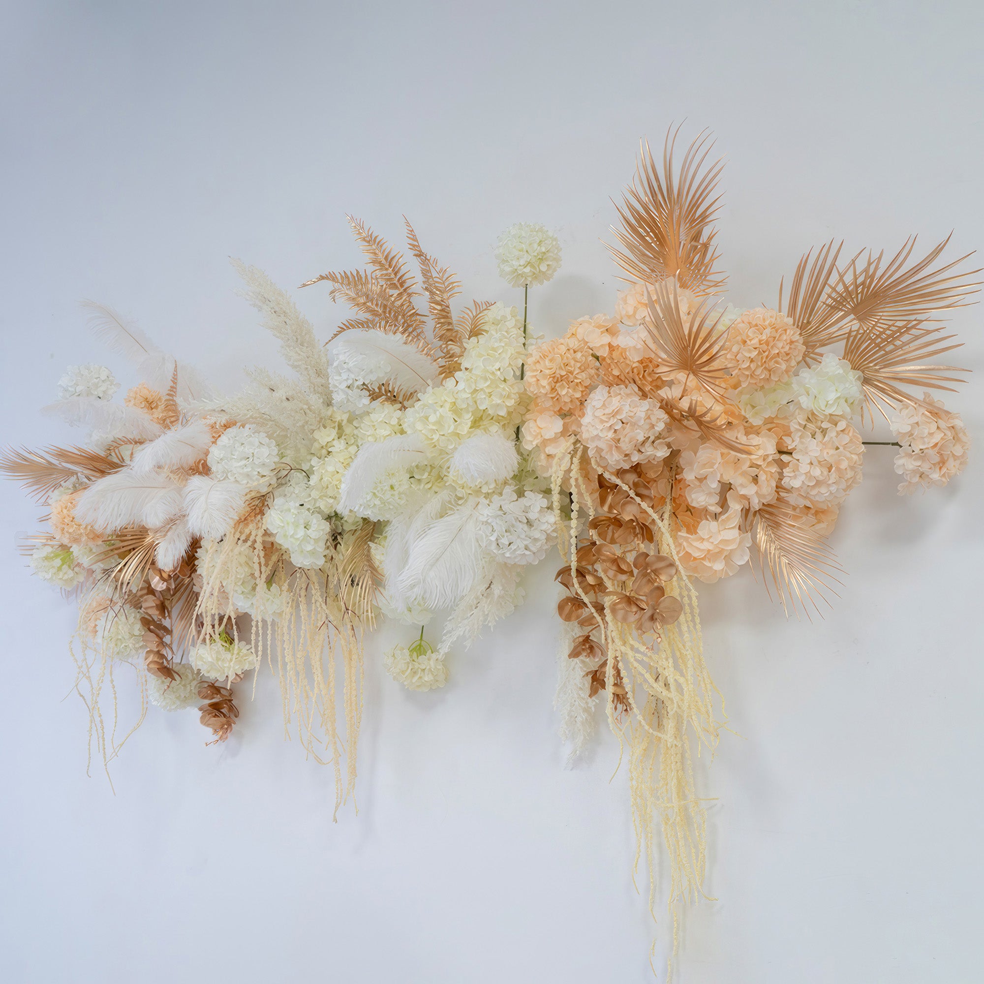 This image features an artificial floral arrangement with hydrangea - like blooms, palm fronds, and feathers. Colors range from white to peach and gold, presenting a luxurious and modern style for event decoration.