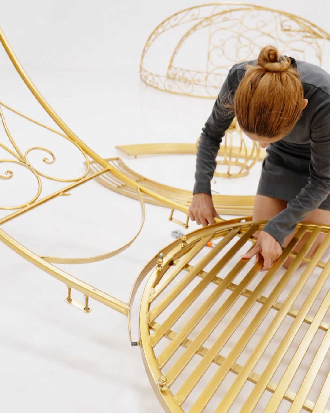 Person assembling a gold metal bed frame on a white background