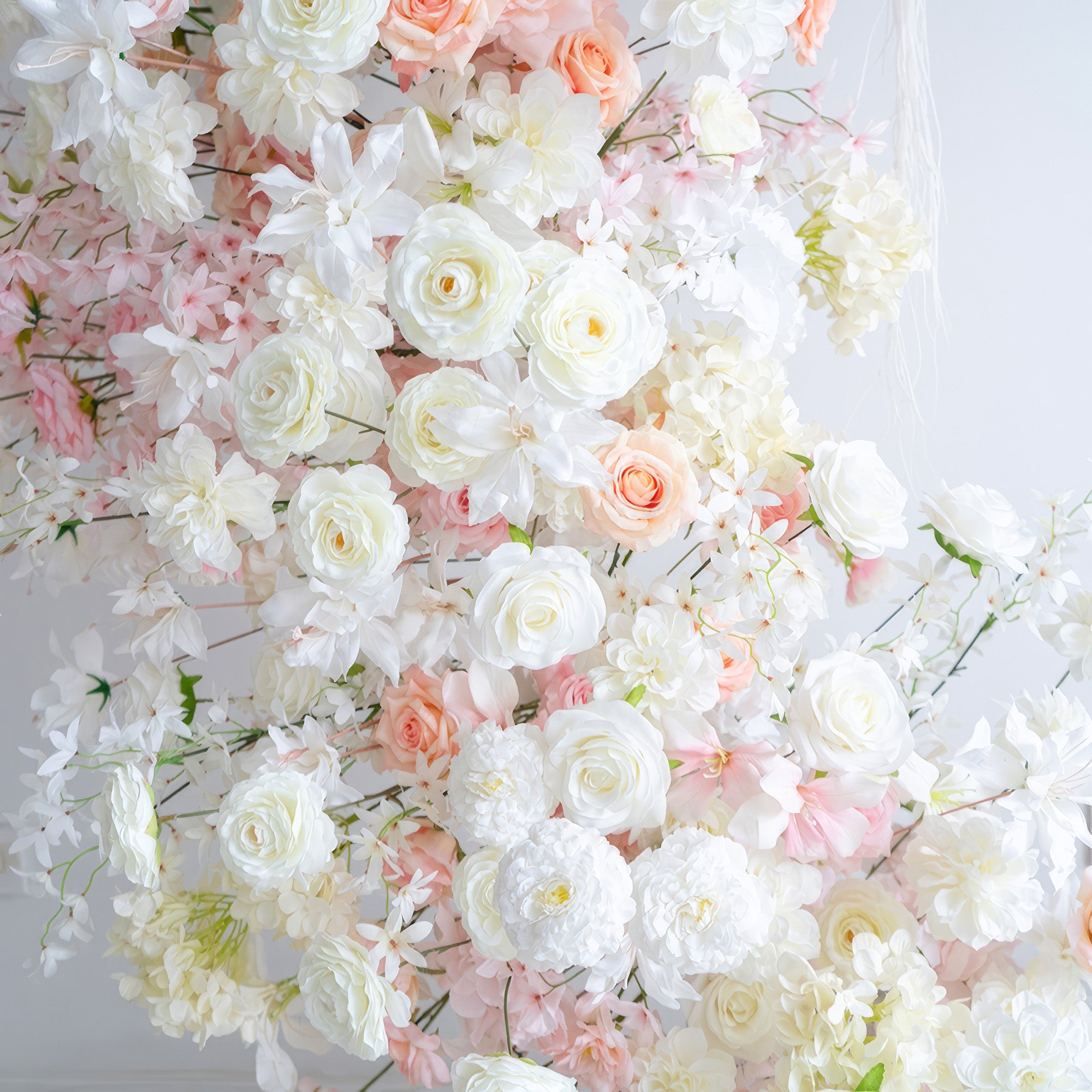 This image showcases an arrangement of artificial flowers in soft hues of white, light pink, and peach. It includes roses and chrysanthemums. The style is gentle and romantic, evoking a sense of elegance.