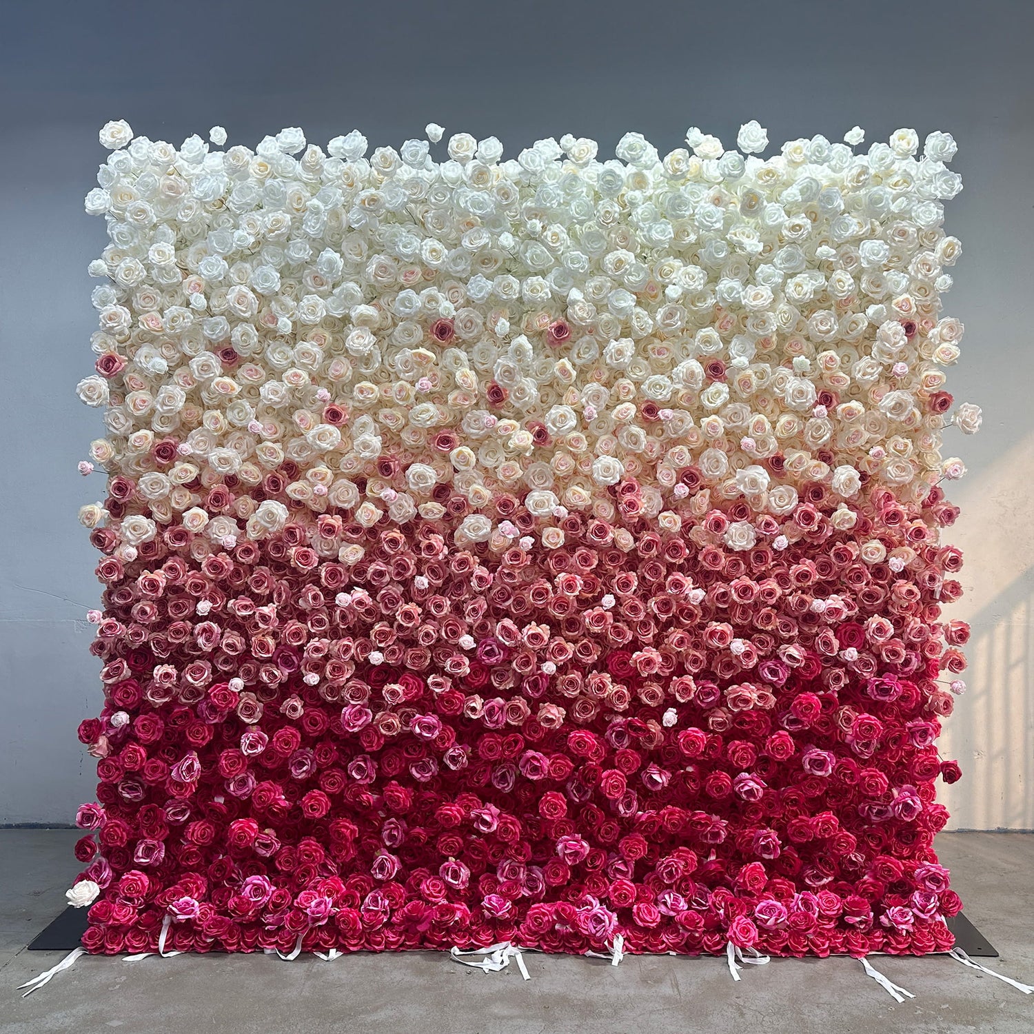 This image showcases a large flower wall densely covered with artificial roses. The wall features a gradient color scheme that transitions from pure white at the top, gradually moving through shades of light pink, deeper pink, and finally to a rich magenta at the bottom. The style is elegant and visually striking, making it ideal for events like weddings or photo - backdrops, creating a romantic and luxurious atmosphere.