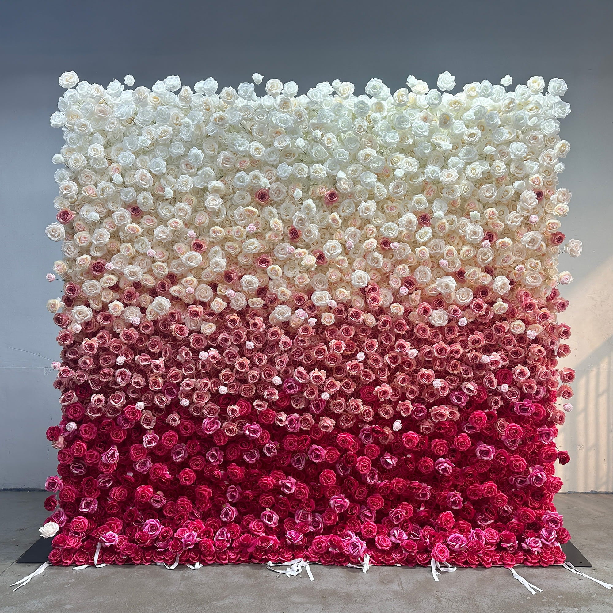 This image showcases a large flower wall densely covered with artificial roses. The wall features a gradient color scheme that transitions from pure white at the top, gradually moving through shades of light pink, deeper pink, and finally to a rich magenta at the bottom. The style is elegant and visually striking, making it ideal for events like weddings or photo - backdrops, creating a romantic and luxurious atmosphere.