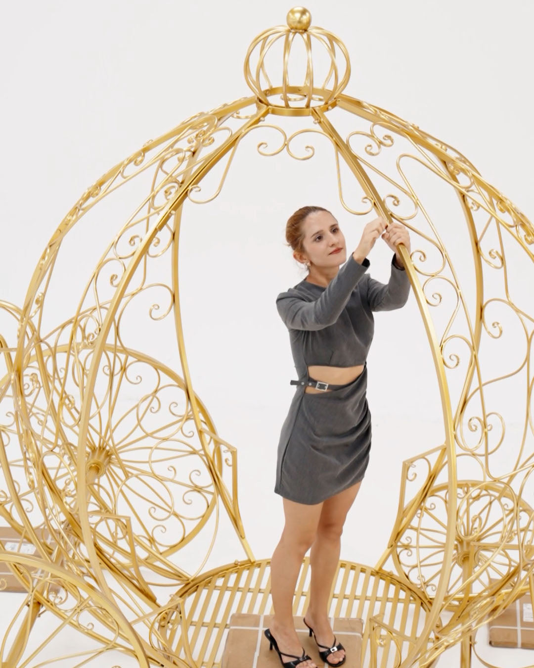 Woman standing inside a large decorative gold birdcage against a white background