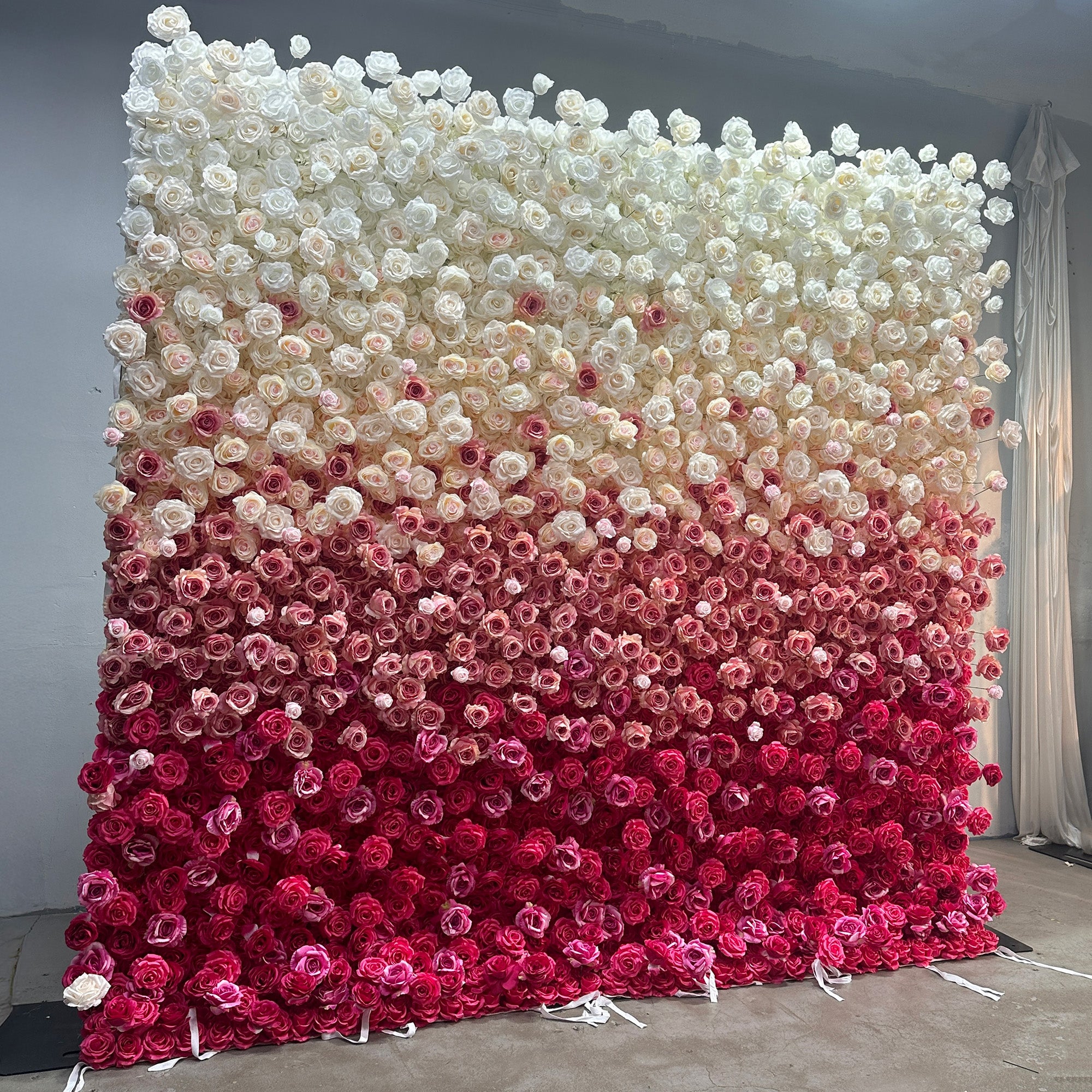 This image showcases a stunning flower wall crafted by ValarFlowers. The wall is densely adorned with artificial roses, arranged in a gradient pattern. The colors transition seamlessly from pure white at the top, through soft pinks and peaches, to deep magenta at the bottom. The overall style is elegant and romantic, making it an ideal backdrop for events such as weddings or photo - shoots.