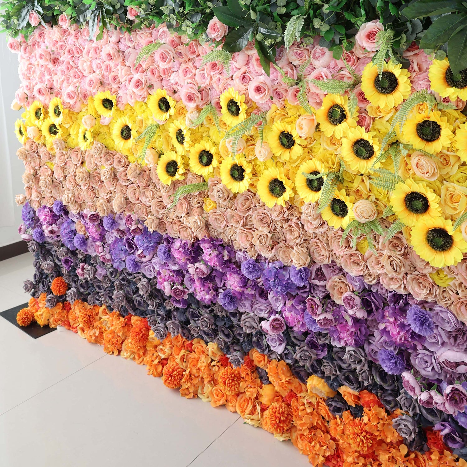 ValarFlowers presents a floral wall with an array of artificial roses, sunflowers, hydrangeas, and other blooms in a colorful, layered arrangement.