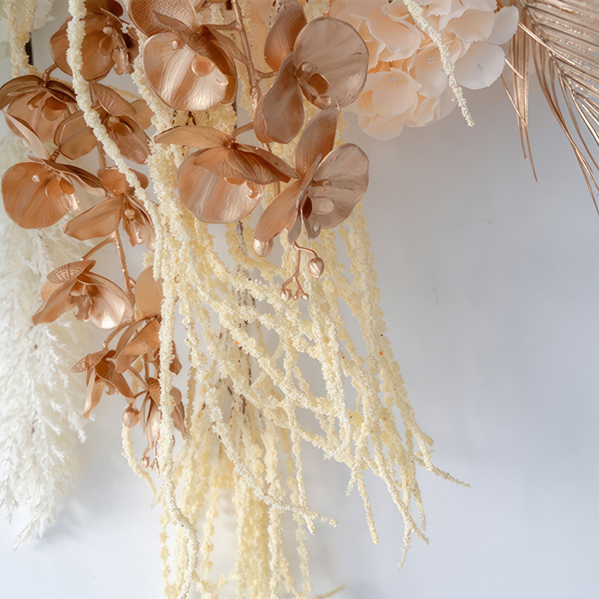 This image shows artificial flowers including orchids in a metallic copper - brown shade, along with trailing cream - colored elements. The style is elegant and modern, with a touch of luxury.