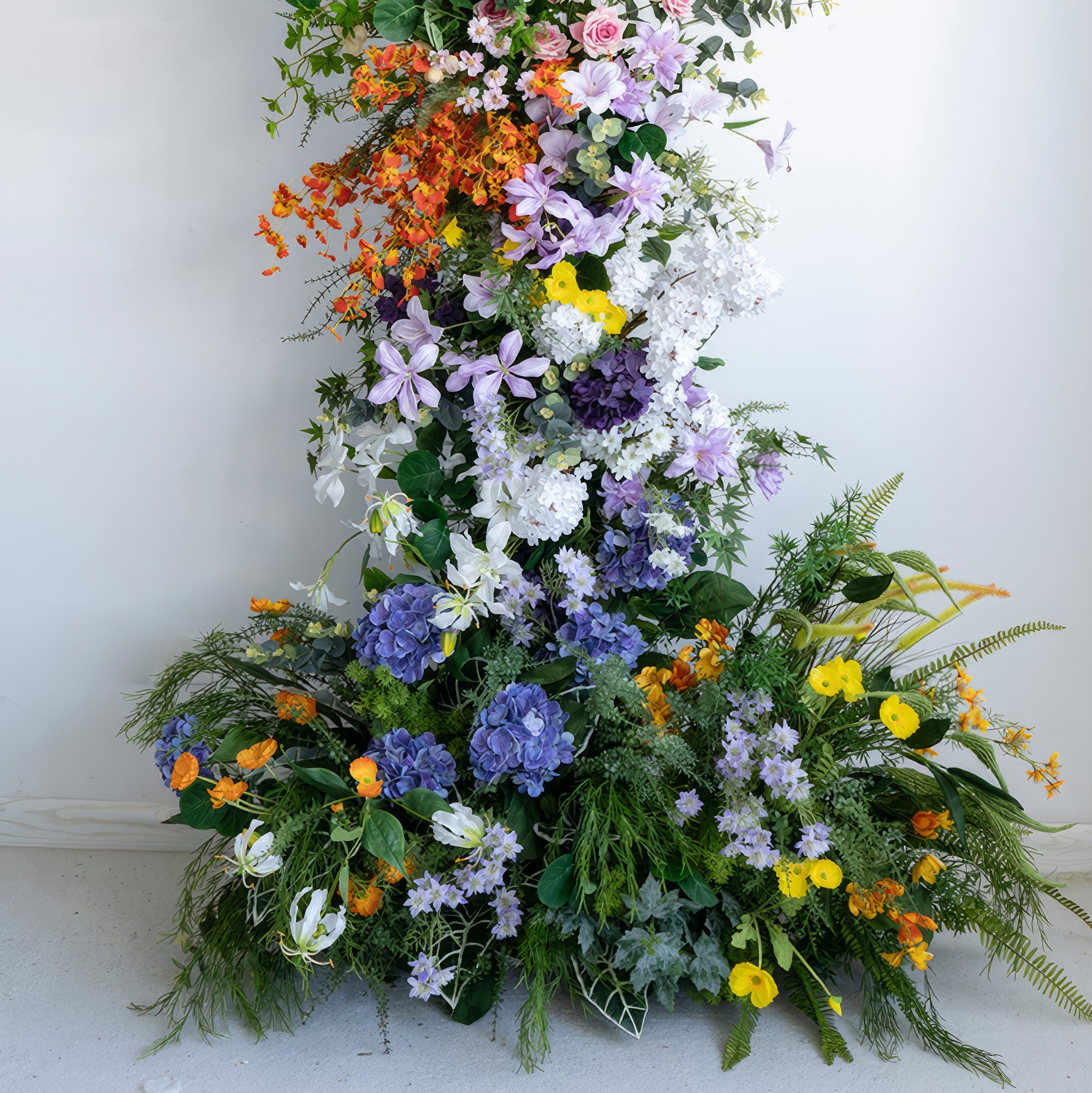 This artificial flower arrangement features a rich color palette of orange, purple, white, yellow, and various shades in between. It includes large hydrangeas, delicate purple blooms, and bright orange accents. The overall style is vivid and nature - inspired, creating a lush and eye - catching display.