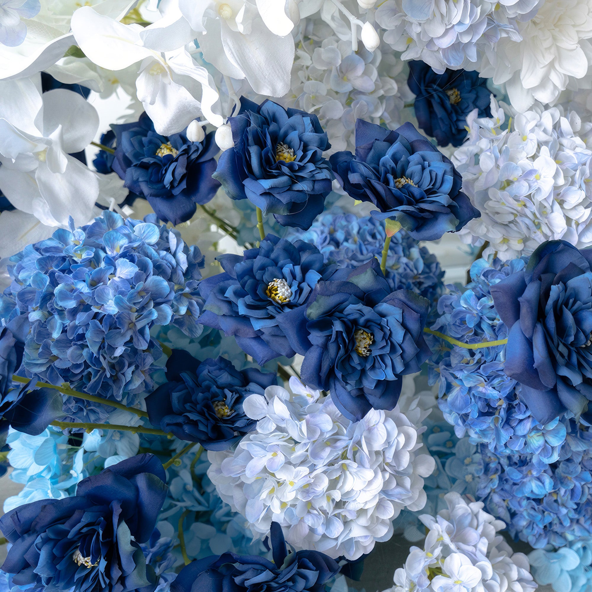 This arrangement showcases a harmonious blend of deep blue roses, various shades of blue hydrangeas, and white blooms. Exuding a serene and elegant style, it&
