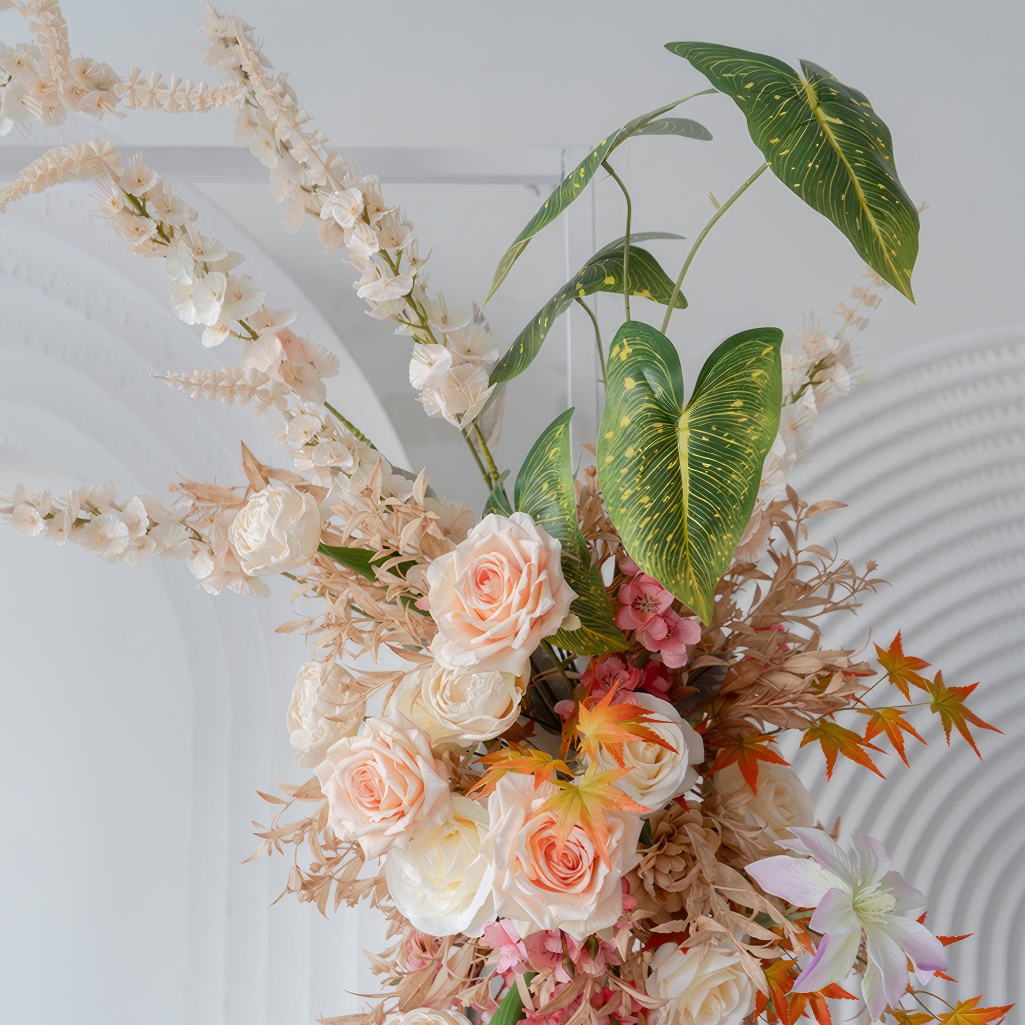 This image showcases an artificial flower arrangement with roses as the main flower, along with other blooms and large - veined leaves. Colors include soft peach, white, pink, and hints of orange, in a romantic, natural style.