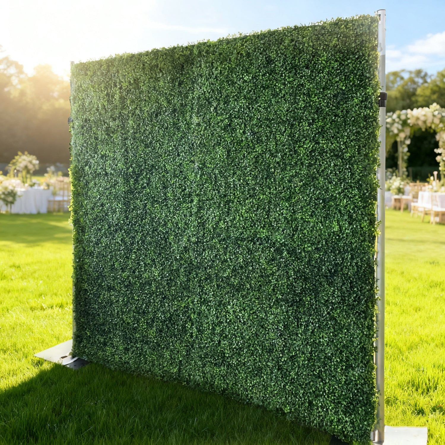 This image showcases a lush artificial greenery wall by ValarFlowers, set outdoors on a vibrant lawn. It features dense, uniform green foliage, creating a rich, natural, and visually refreshing display. Bathed in sunlight, this piece is perfect for adding organic elegance to events, exuding a serene and sophisticated atmosphere.