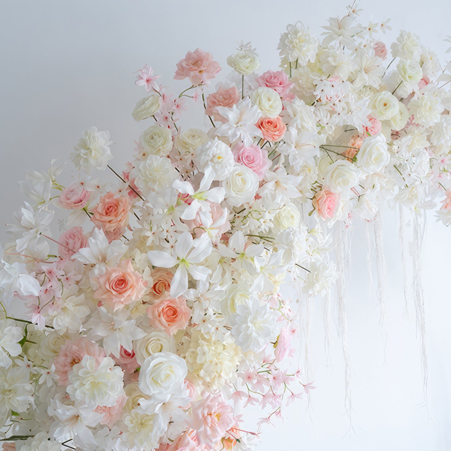 This image features an artificial flower arrangement with roses and various blossoms in soft white, light pink, and peach tones. The style is romantic and elegant, perfect for a dreamy event setting.