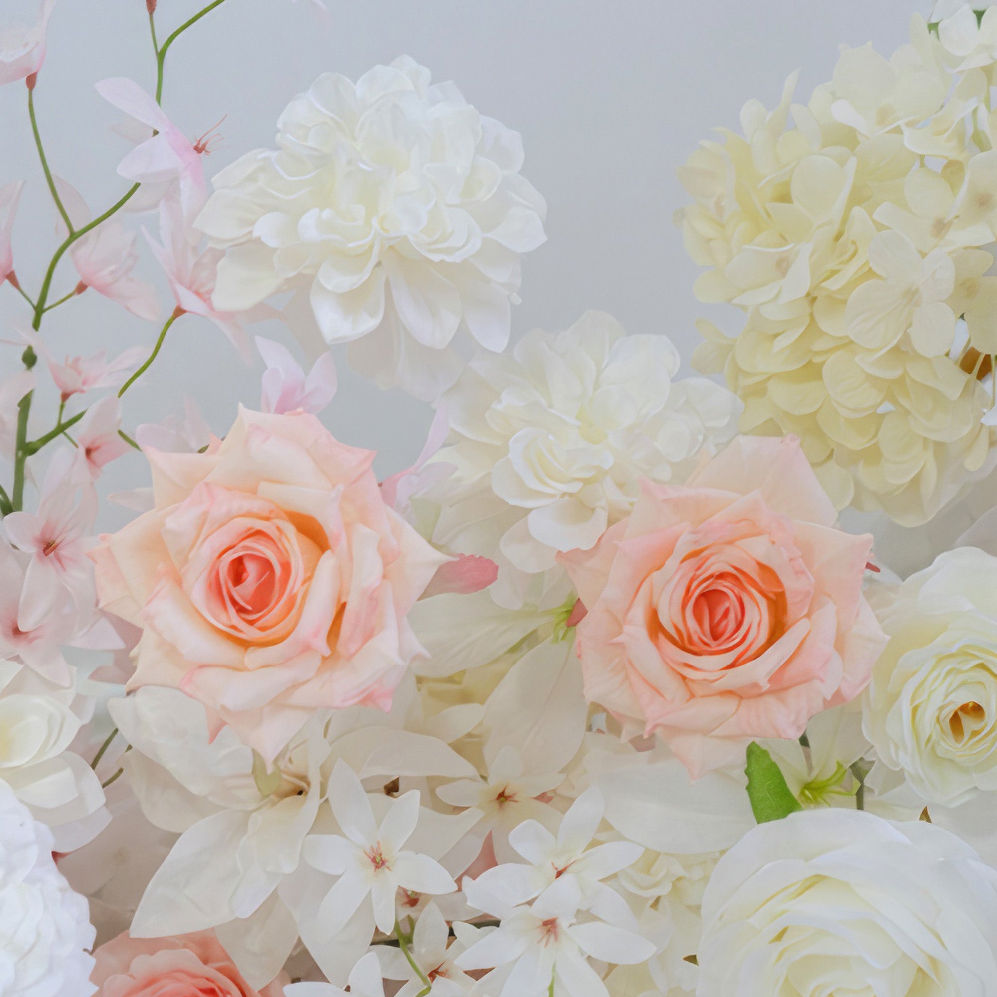 This image shows an arrangement of artificial flowers including roses and hydrangeas. Colors range from soft white and cream to light peach. The style is delicate and romantic, ideal for a charming decor.