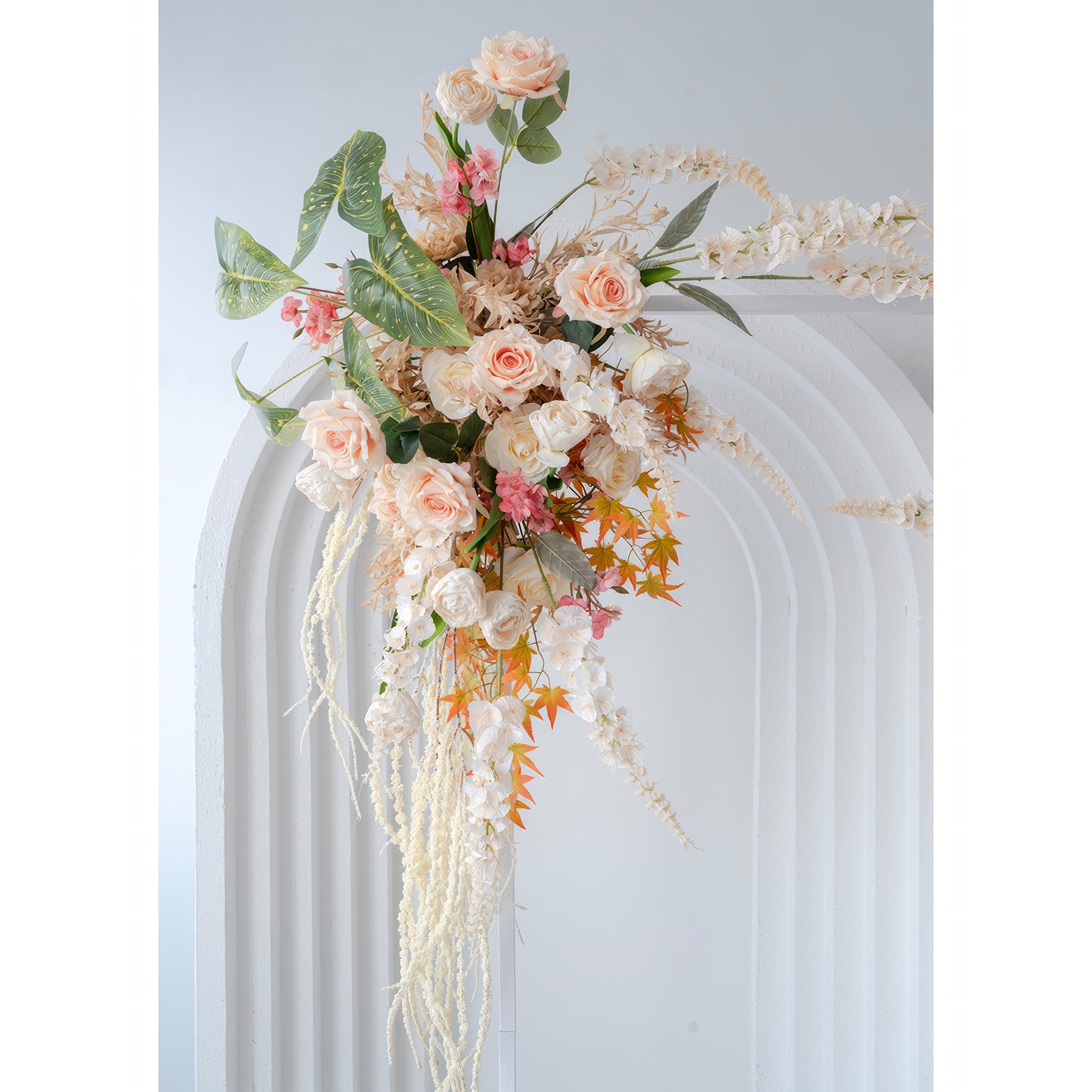 This image shows an artificial floral arrangement on an arch. It features roses, small pink flowers, and some with long white petals. Colors include soft peach, white, pink, and orange - hued leaves, in a romantic, natural style.
