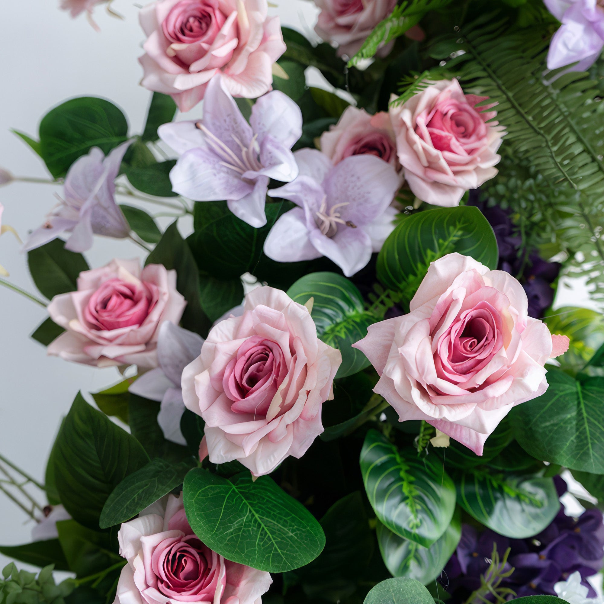 This image features an artificial flower arrangement with soft pink roses as the focal point, complemented by light purple lilac - like flowers and lush green leaves. The color palette is gentle and romantic, creating an elegant and charming style.