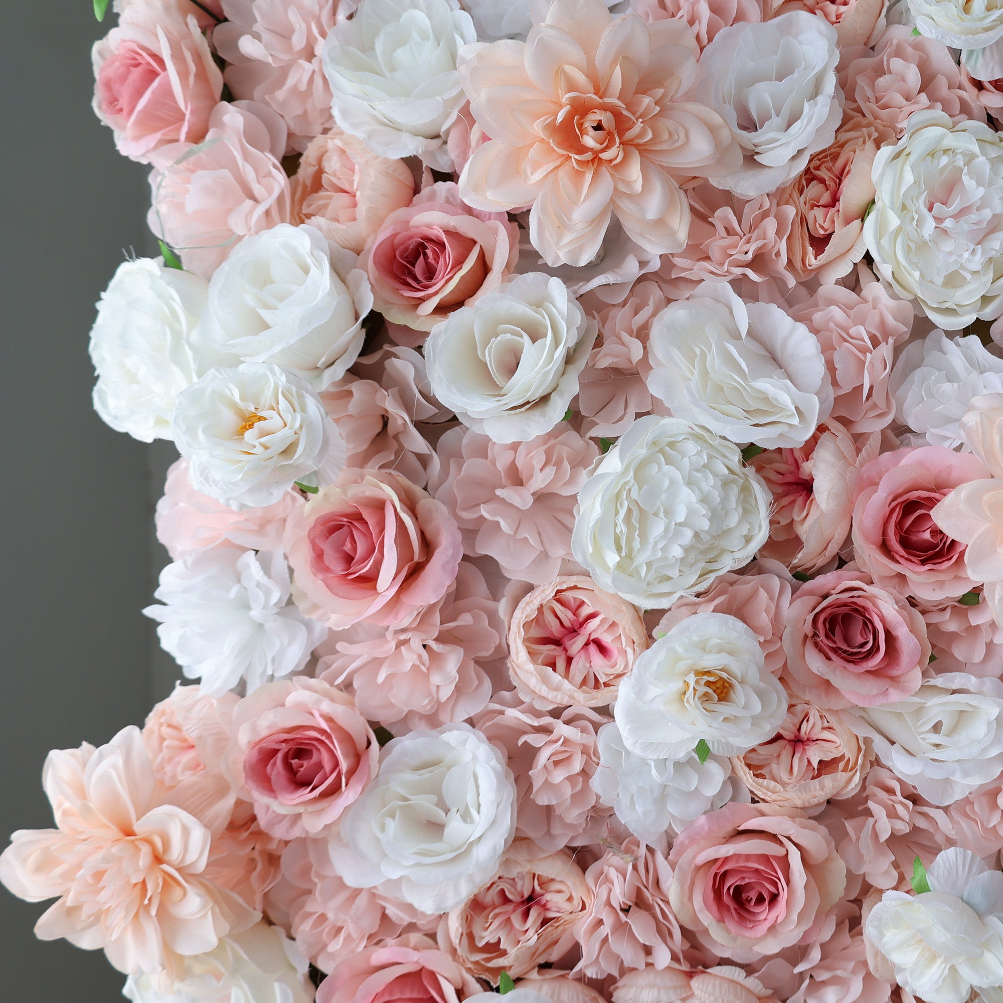 A dense arrangement of artificial flowers showcases a beautiful mix of pink, blush, and white blooms. Various floral types, including roses and other delicate blossoms, create a lush, romantic display. The soft color palette and intricate detailing give off an elegant, charming vibe, perfect for events like weddings, photo backdrops, or upscale gatherings needing a sophisticated floral focal point.