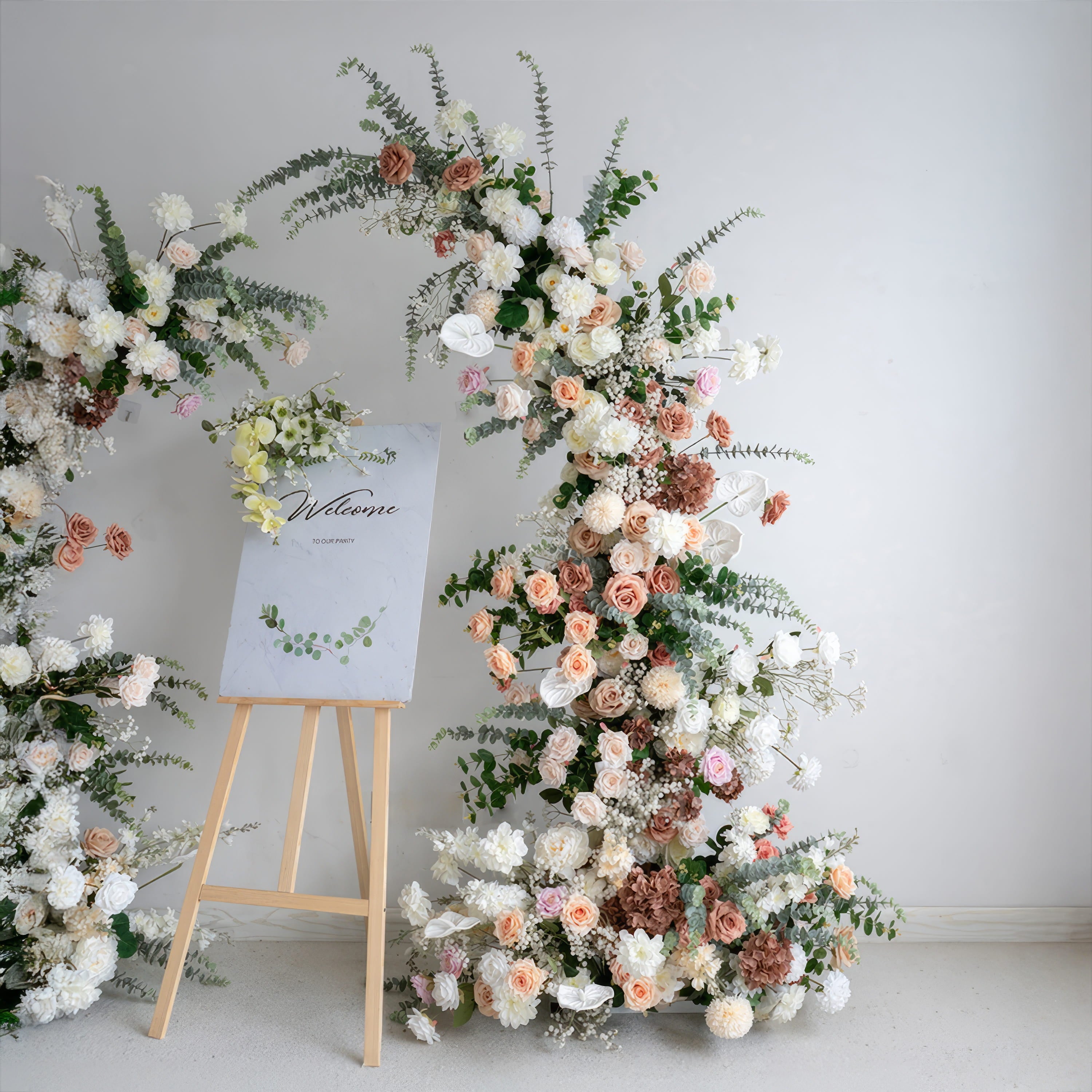A romantic, asymmetrical floral arch from Valar Flowers, crafted with a soft, warm palette of blush pink, terracotta, and creamy white blooms—including roses, peonies, and delicate baby&