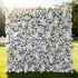 This image showcases a stunning floral wall by Valar Flowers, densely adorned with an array of white and light - hued roses and other blooms. Set outdoors on a lush green lawn with trees in the background, the vibrant arrangement exudes elegance and natural beauty, creating a picturesque and romantic atmosphere, perfect for special events or as a captivating decorative backdrop.