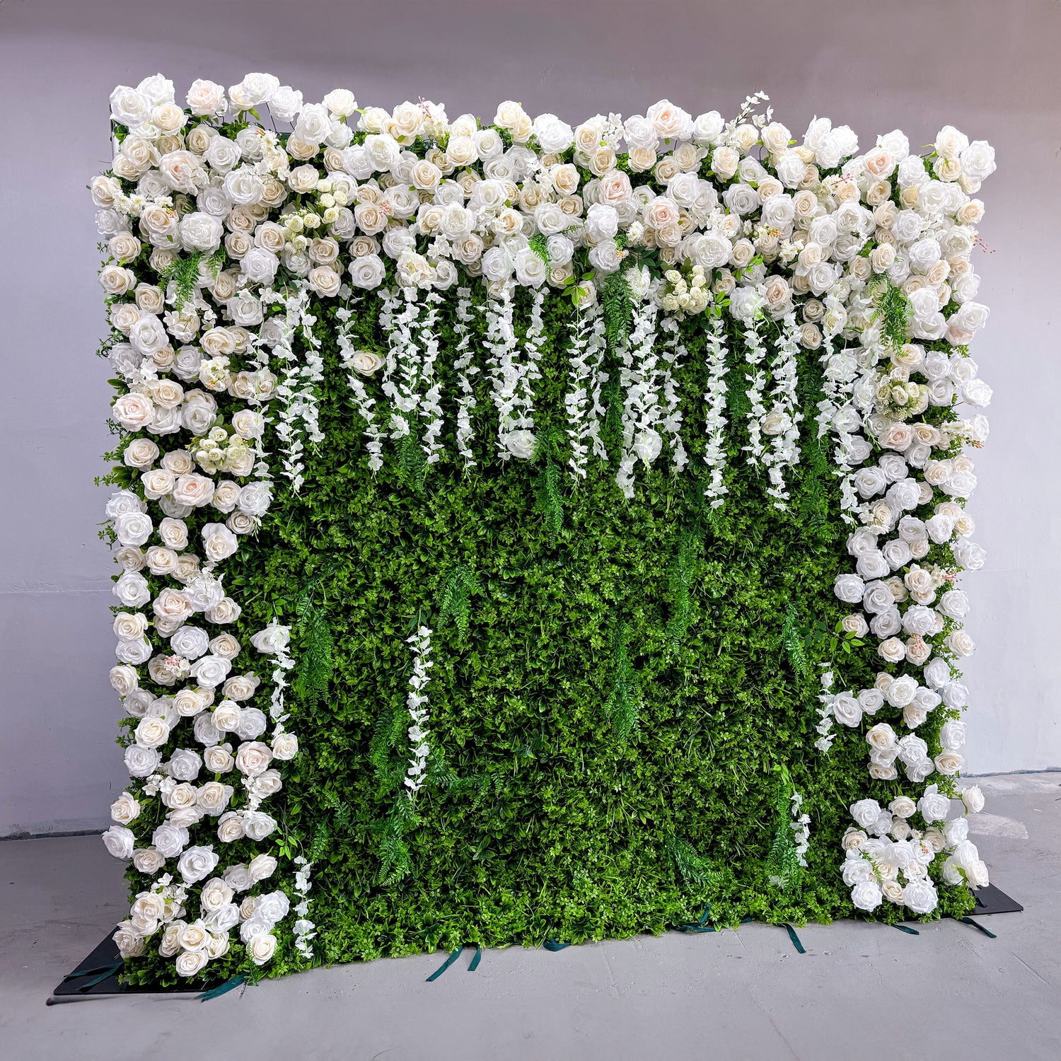 This flower wall backdrop is a stunning display. It features an arch - shaped design with a lush, green base covered in dense foliage. The top and sides are adorned with an abundance of large, white roses, creating a romantic and elegant atmosphere. Cascading white floral strands add a touch of grace, enhancing the overall grand and luxurious look of the backdrop.
