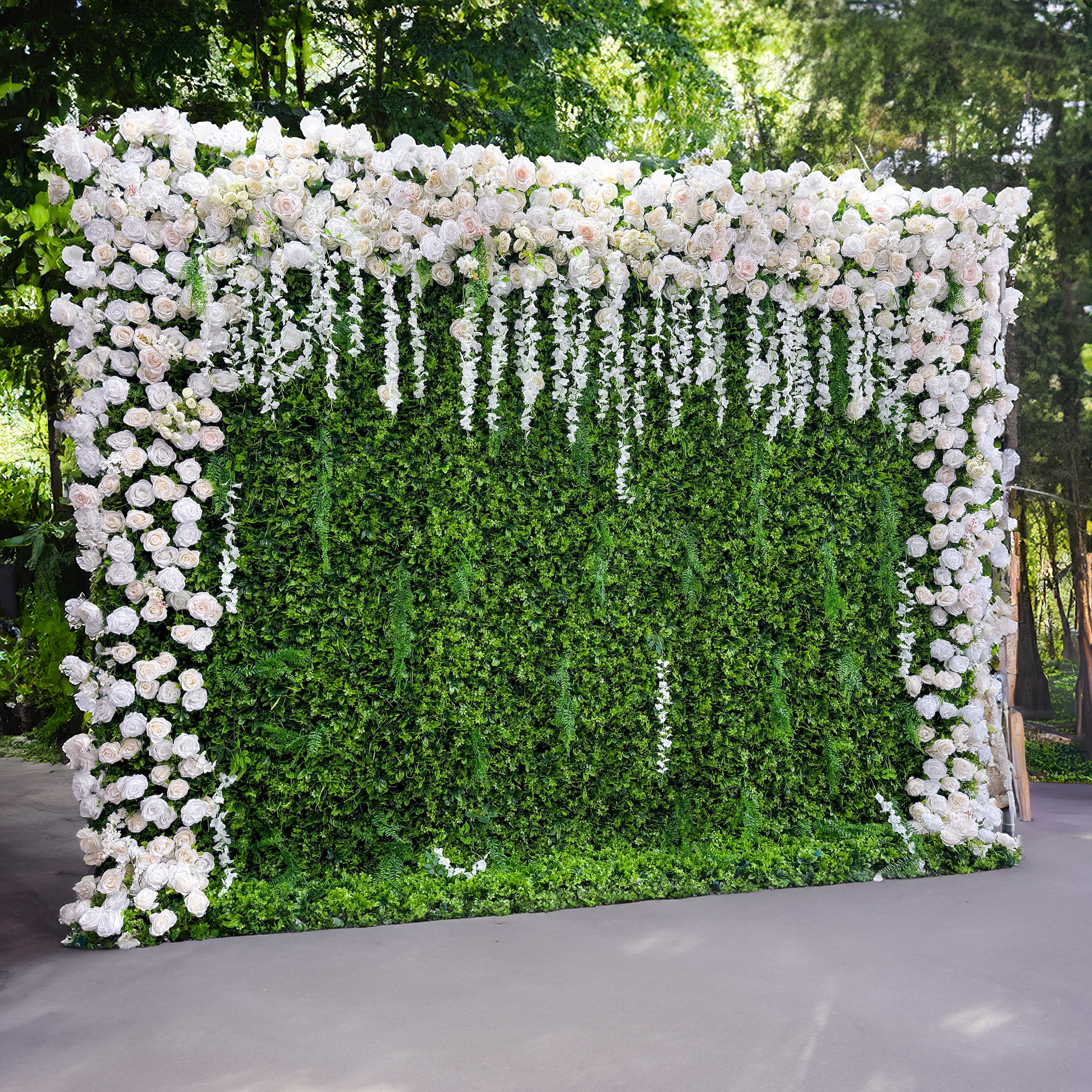 This flower wall is a lush green backdrop adorned with abundant white roses. The roses are densely packed, creating a rich and luxurious appearance. Additionally, there are cascading white floral strands hanging down, adding a touch of elegance and movement to the overall design.