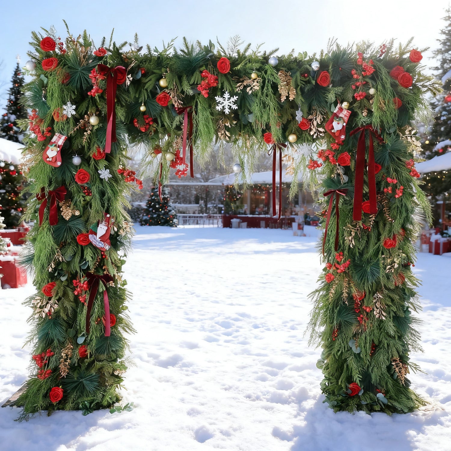 This image showcases a festive Christmas arch set in a snowy outdoor scene. Adorned with lush green foliage, vibrant red roses, and classic Christmas decorations like stockings, snowflakes, and baubles, the arch exudes holiday cheer. In the background, decorated Christmas trees and a clear blue sky enhance the joyful, wintry atmosphere, perfect for Christmas celebrations.