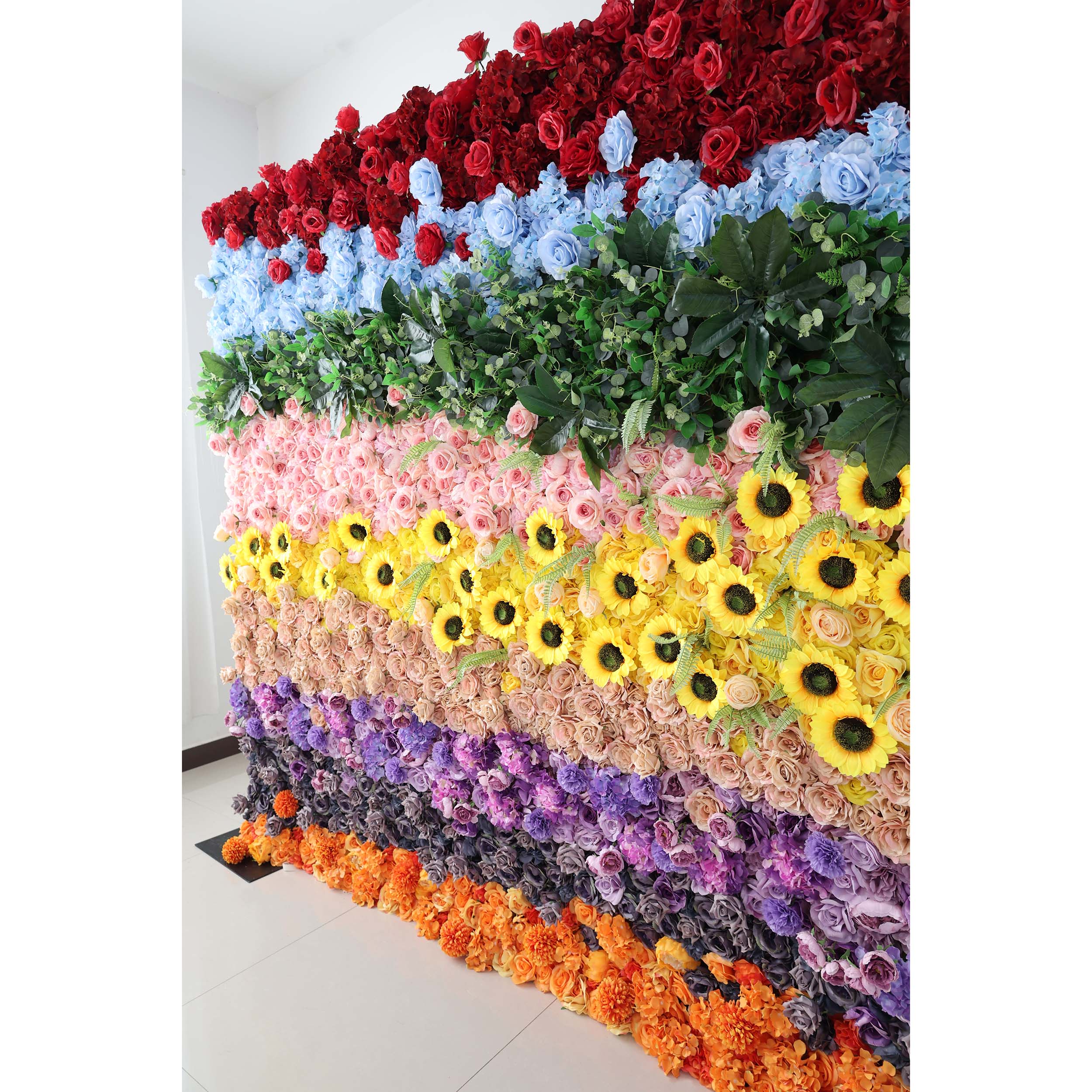 A vibrant floral wall by ValarFlowers, showcasing a mix of artificial roses, sunflowers, and other blooms in a spectrum of colors.