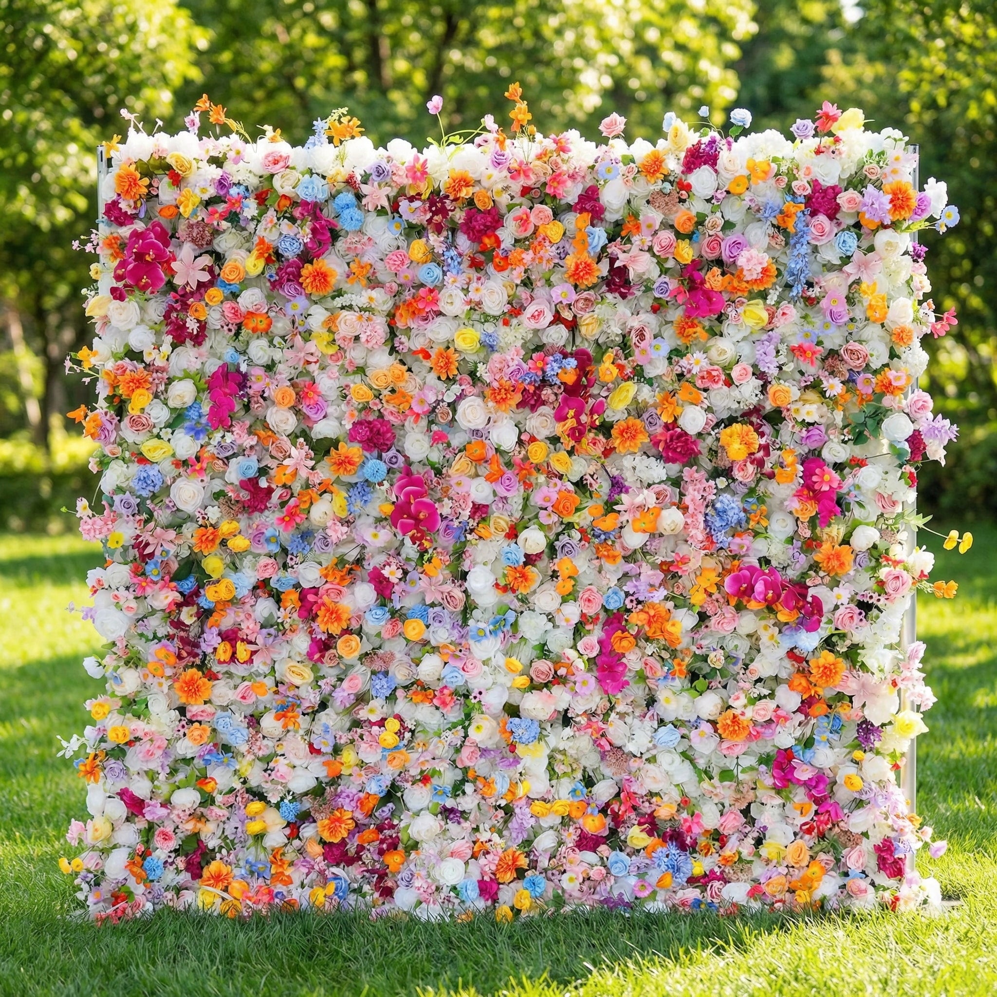 This vibrant flower wall from Valar Flowers is a dense, joyful tapestry of blooms in every hue—roses, daisies, hydrangeas, and delicate sprigs—creating a lush, rainbow-like backdrop. Set against a sunlit lawn and greenery, it evokes a playful, celebratory atmosphere ideal for weddings, photo booths, or lively events.