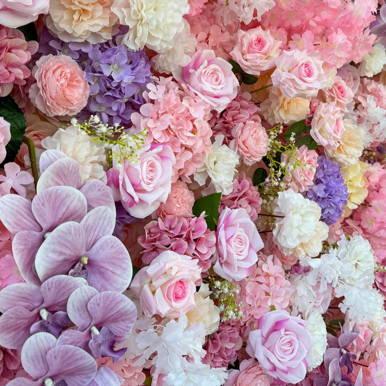 This photo from ValarFlowers showcases a lush floral arrangement. It features roses in soft pink and white tones, hydrangeas in purple and pink, and delicate white flowers with green stems. Large purple orchids add a touch of elegance. Ideal for weddings, bridal showers, or romantic events, this dreamy and colorful mix exudes charm and sophistication, creating a visually stunning backdrop.