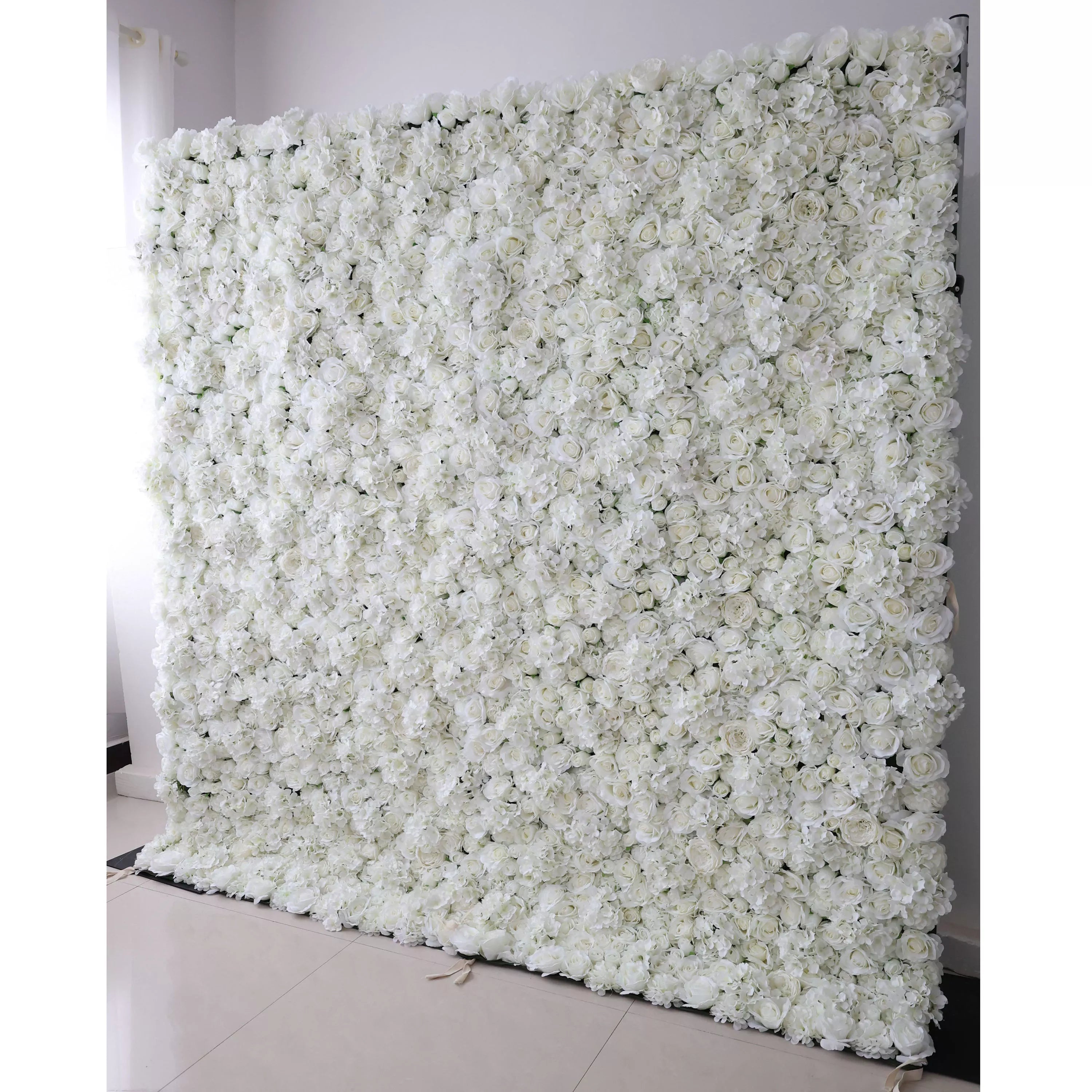 This is a large, rectangular artificial flower wall backdrop from **Valar Flowers**, densely packed with a lush arrangement of white roses, peonies, and delicate filler blooms. It stands upright indoors on a light tiled floor, creating a clean, elegant, and romantic aesthetic ideal for wedding decor, photo shoots, or special event styling.