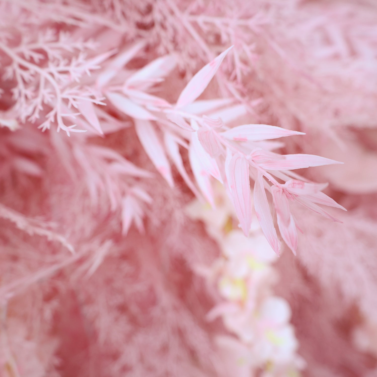 This close - up image showcases delicate artificial pink foliage. The leaves, with their soft pink hues and slender shapes, are part of a dense arrangement. Alongside, there are hints of other light - colored floral elements, creating a cohesive and gentle scene. The overall composition exudes a sense of tranquility and refined beauty, ideal for decorative purposes in events or as a visually appealing artistic display.