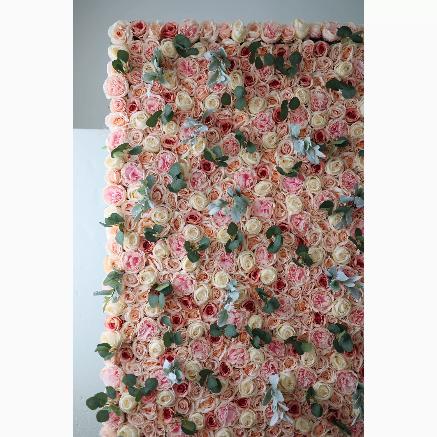 A large artificial flower wall features a harmonious mix of soft - pink, peach, and cream roses. Interspersed are green eucalyptus leaves and light - toned foliage, adding texture. The dense, layered arrangement creates a lush, romantic backdrop, ideal for adding elegance to events.