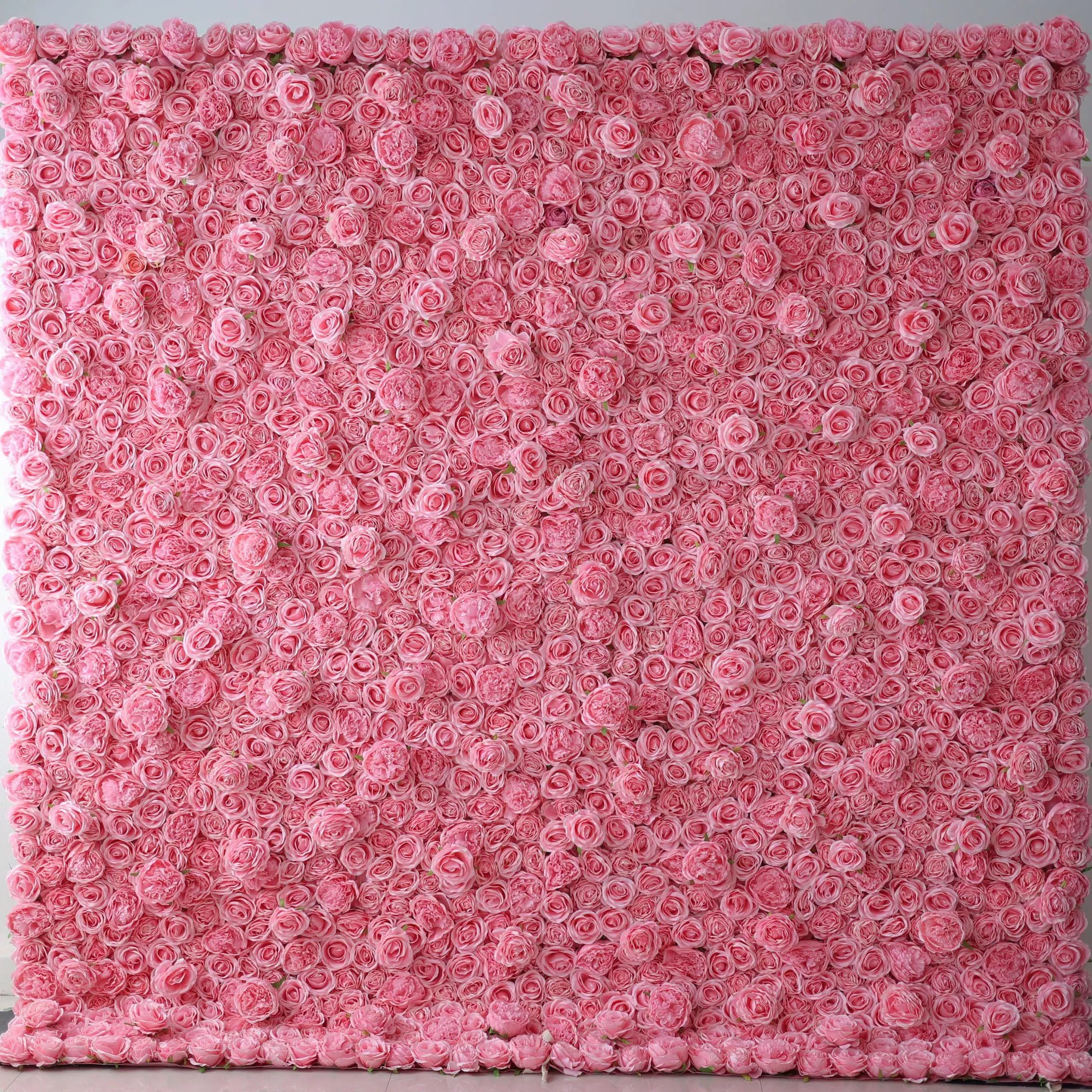 A vast artificial flower wall showcases a dense arrangement of uniform pink roses. Each bloom is tightly clustered, creating a smooth, lush, and romantic texture. The consistent pink hue gives a soft, elegant, and dreamy vibe, perfect for adding a touch of sweetness to decor or event backdrops.