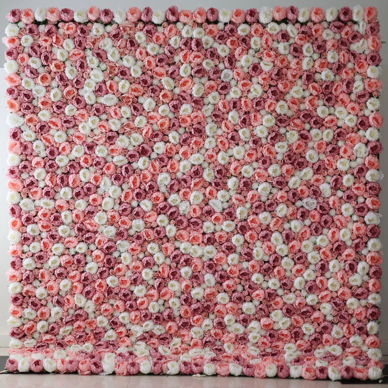 A large artificial flower wall features a mesmerizing pattern of pink, white, and light pink roses. The blooms are densely packed, creating a lush, textured, and visually striking backdrop. The harmonious color blend gives off a romantic, elegant vibe, perfect for adding a decorative touch to events or spaces.