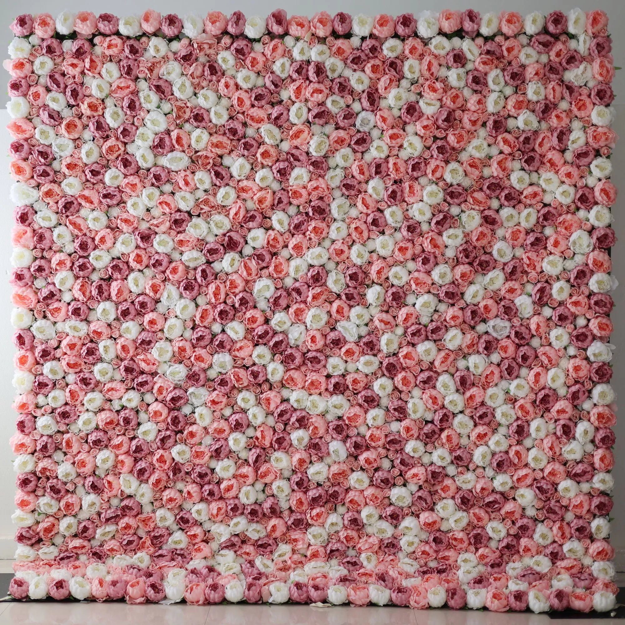 A large artificial flower wall features a mesmerizing pattern of pink, white, and light pink roses. The blooms are densely packed, creating a lush, textured, and visually striking backdrop. The harmonious color blend gives off a romantic, elegant vibe, perfect for adding a decorative touch to events or spaces.