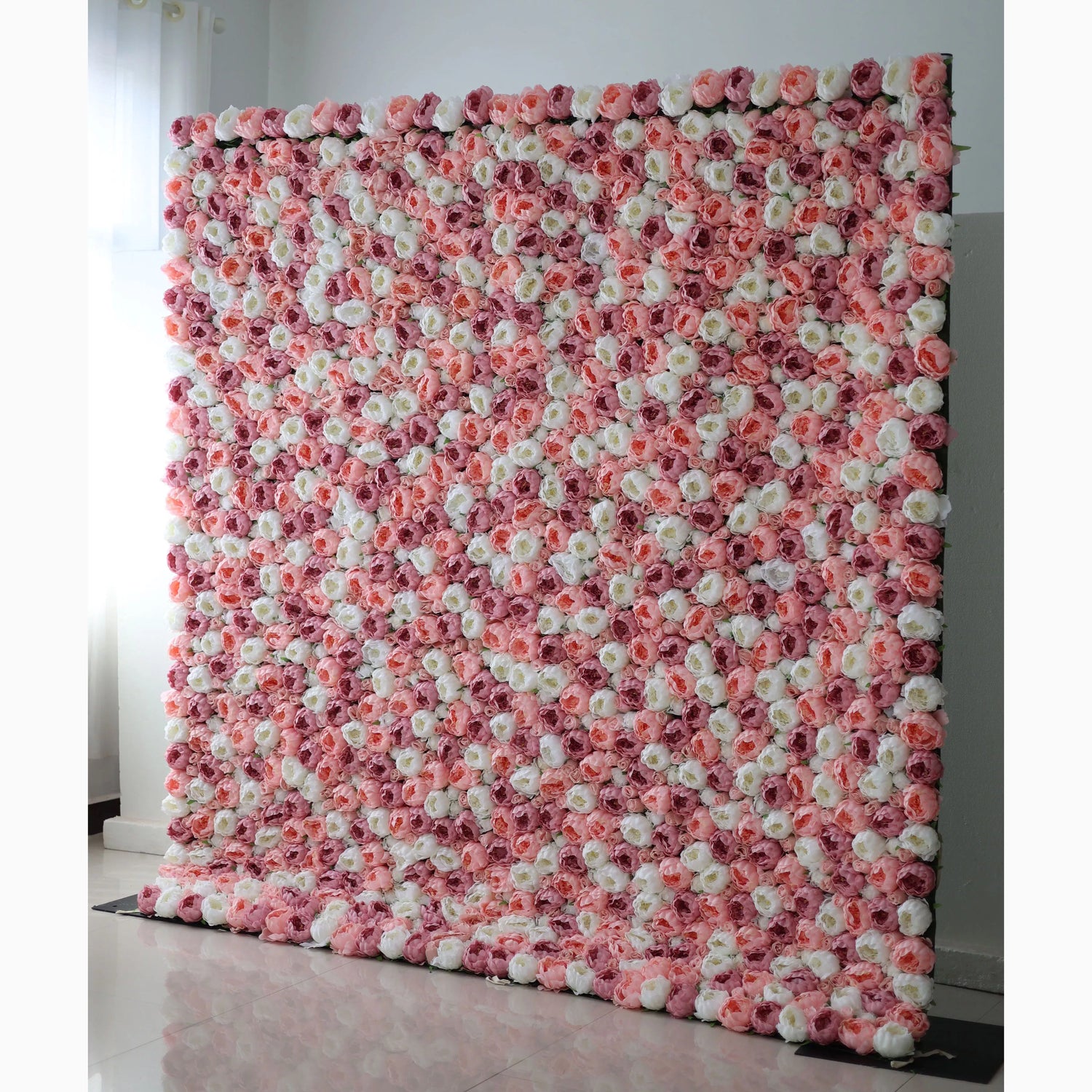 A large artificial flower wall displays a stunning pattern of pink, white, and light pink roses. The blooms are densely packed, creating a lush, textured, and visually striking backdrop. The harmonious color blend gives off a romantic, elegant vibe, perfect for adding a decorative touch to events or spaces.