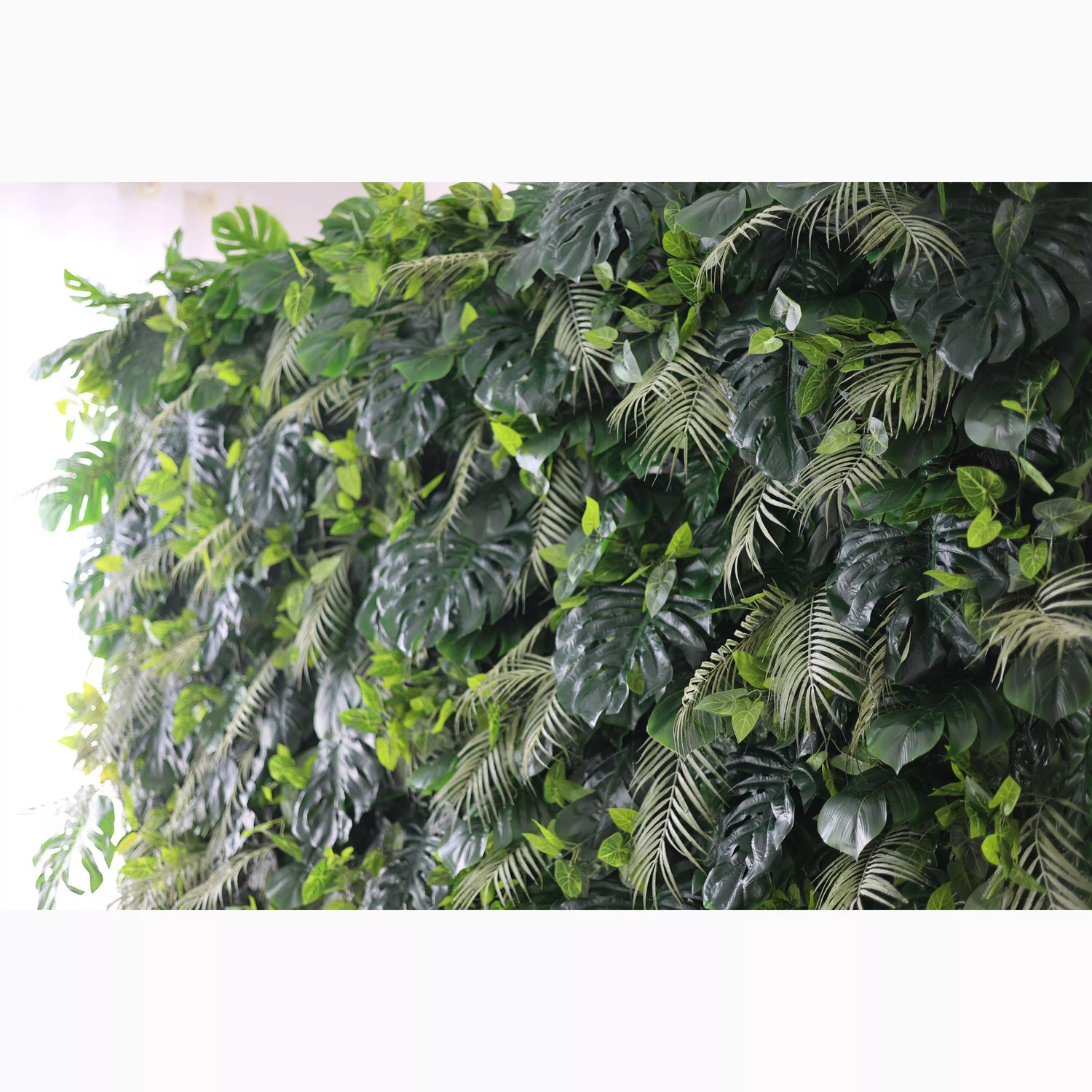 A large artificial greenery wall showcases a dense mix of lush leaves. Big monstera leaves and delicate fern - like fronds in various shades of green create a vibrant, tropical - inspired texture. It’s a fresh, natural - looking backdrop, perfect for adding an organic touch to decor or events.