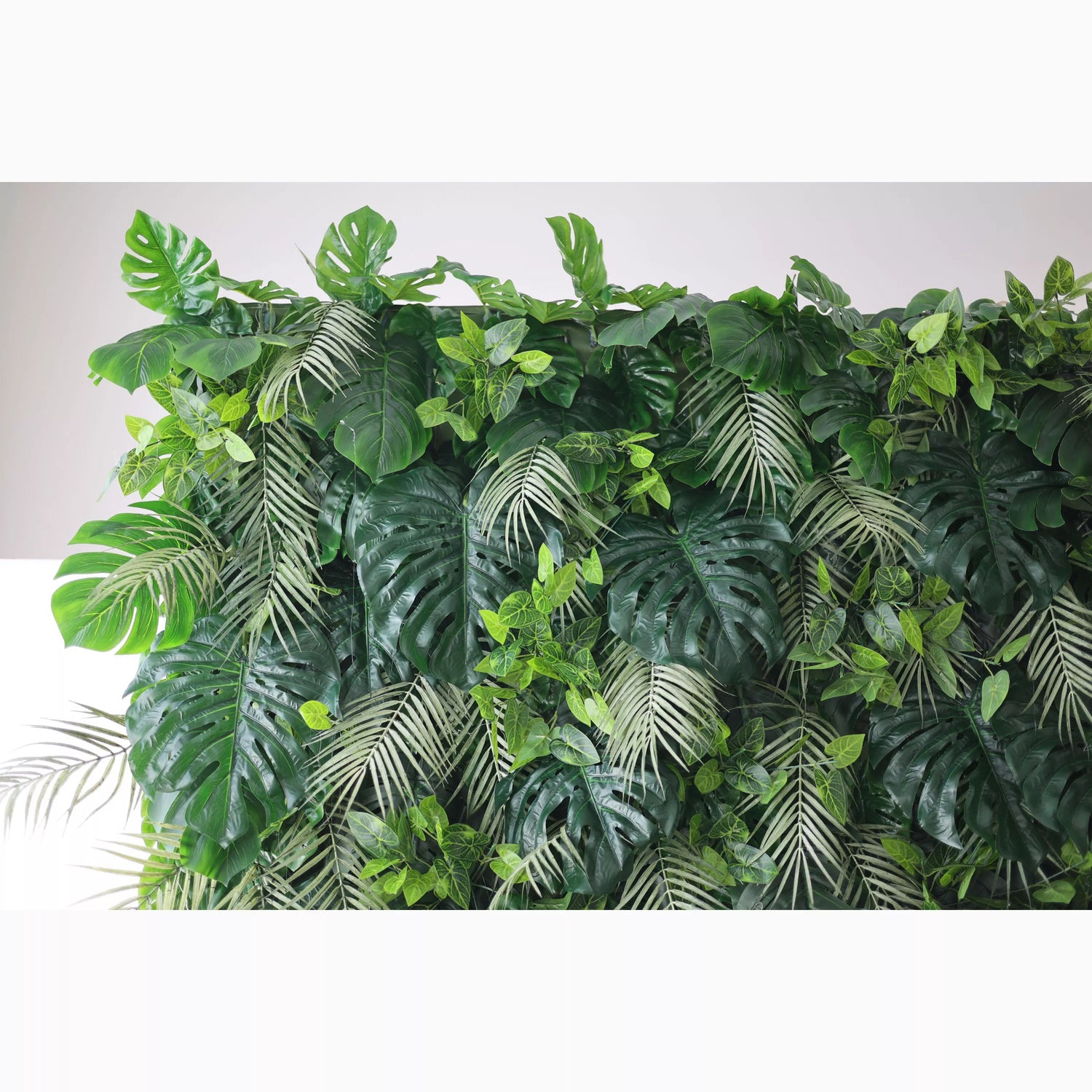 A lush artificial greenery wall features large monstera leaves, delicate fern fronds, and small green foliage. In various shades of green, they create a dense, tropical - inspired texture, bringing a fresh, natural vibe, ideal for adding an organic touch to decor.