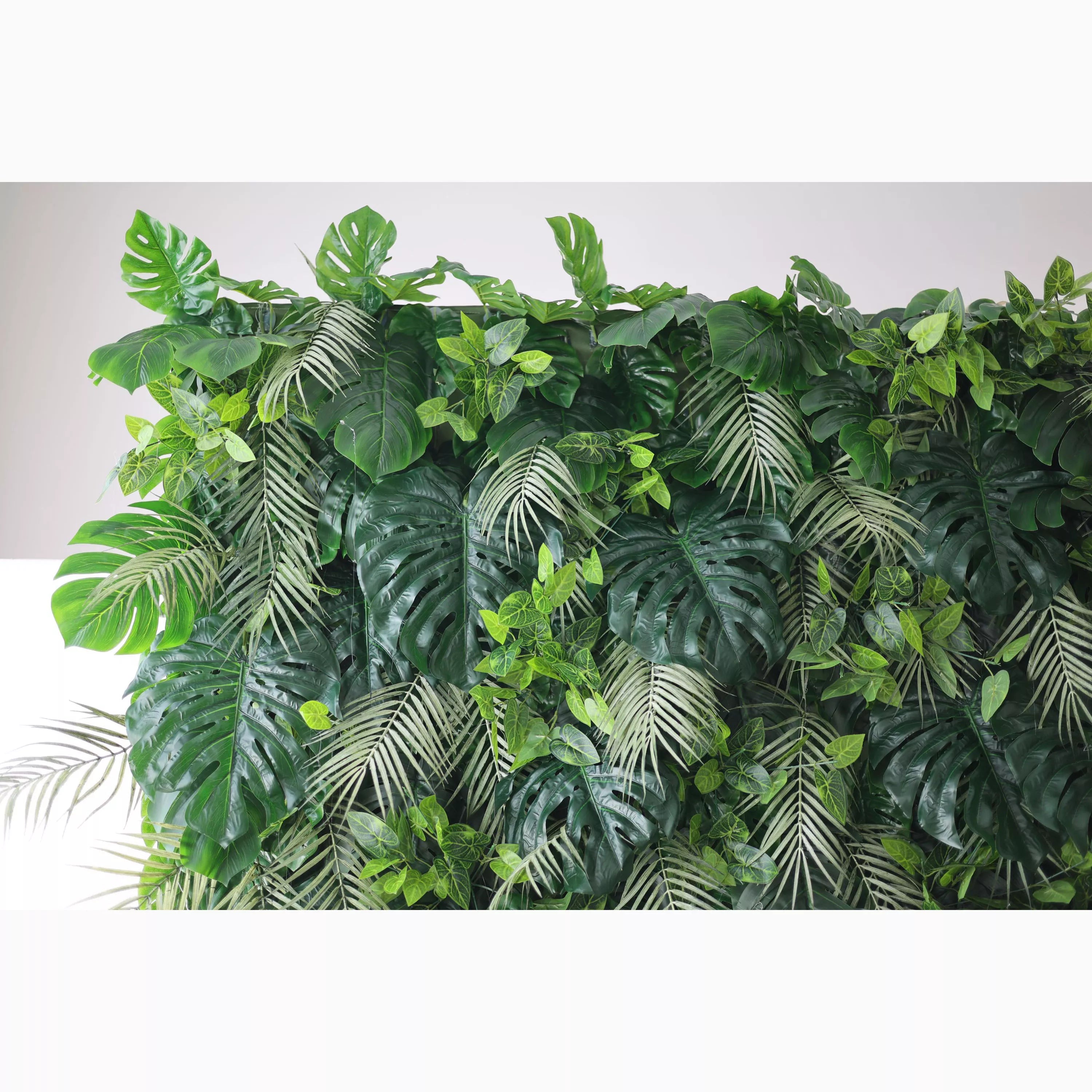 A lush artificial greenery wall features large monstera leaves, delicate fern fronds, and small green foliage. In various shades of green, they create a dense, tropical - inspired texture, bringing a fresh, natural vibe, ideal for adding an organic touch to decor.