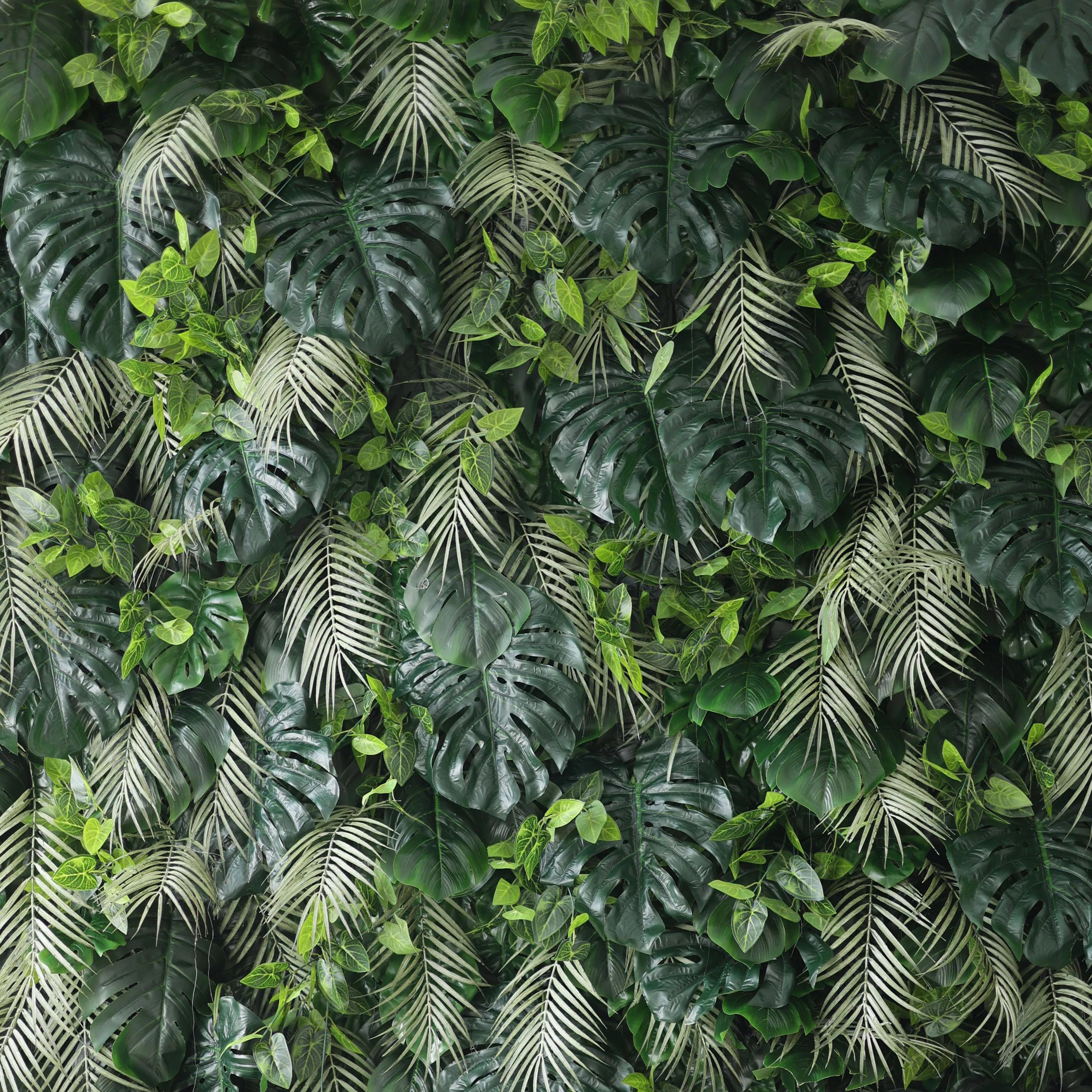 A lush artificial greenery wall features large monstera leaves, delicate fern fronds, and small green foliage. In various shades of green, they create a dense, tropical - inspired texture, bringing a fresh, natural vibe, ideal for adding an organic touch to decor.
