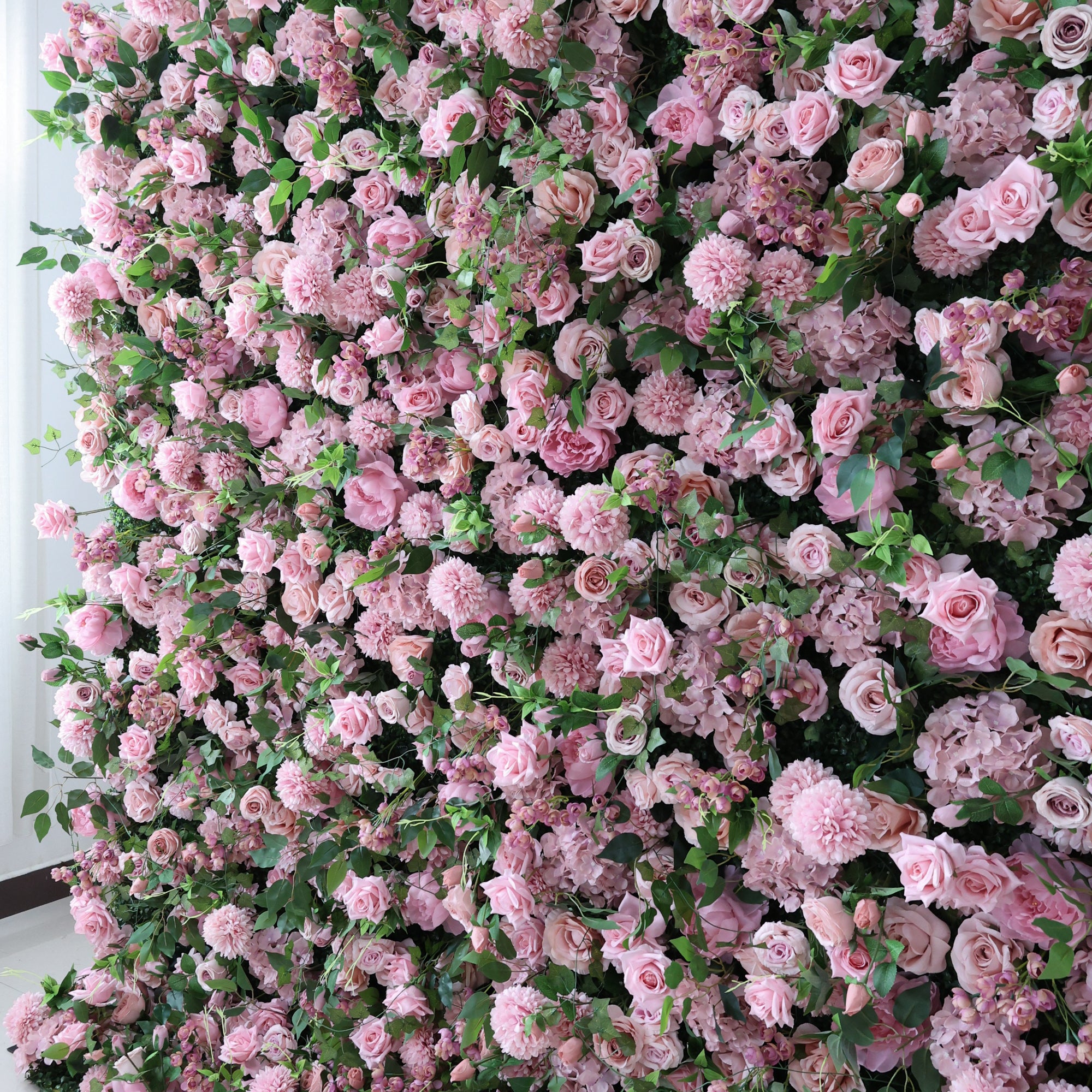 This image showcases a dense, vibrant arrangement of artificial pink flowers, including roses and other blooms, interspersed with lush green leaves. The flowers create a rich, romantic tapestry, exuding elegance and charm. Perfect for decorative use in events or as an eye-catching interior backdrop, the scene blends soft pink hues and natural - looking foliage to form a visually appealing floral display.