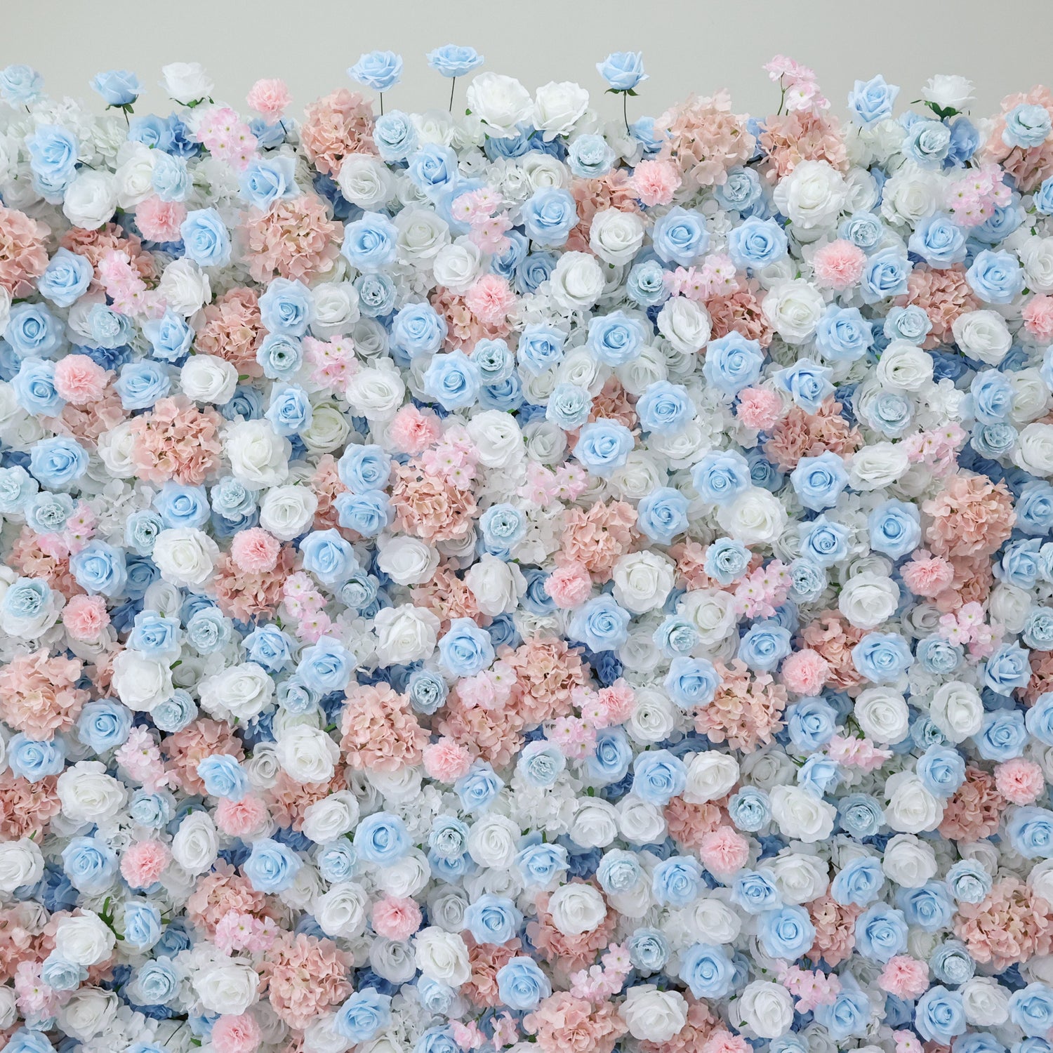 This image presents a dense, vibrant arrangement of artificial flowers in soft pastel shades. Featuring hues of blue, white, and pink, the blooms—including roses and hydrangeas—are clustered tightly to form a lush, romantic floral tapestry. Set against a plain backdrop, the intricate petals and harmonious color palette create an elegant, charming scene, ideal for event decor or as a visually appealing artistic display.