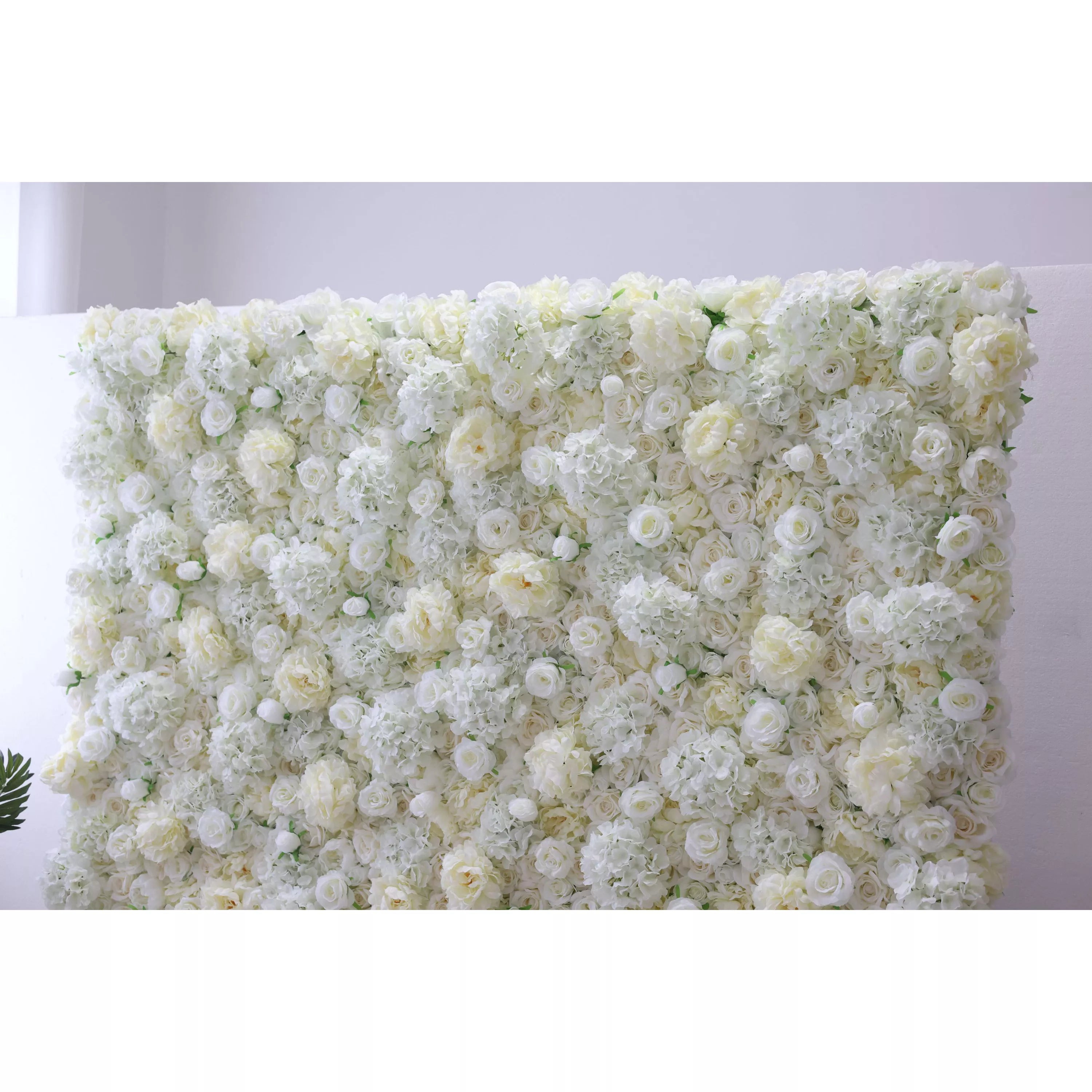 This elegant indoor floral backdrop features a dense, velvety arrangement of artificial white and cream roses, layered with delicate filler blooms to create a lush, three-dimensional texture. Its soft, luminous palette exudes timeless sophistication and romance, making it a stunning focal point for weddings, engagement photos, or upscale events against a minimalist white wall.